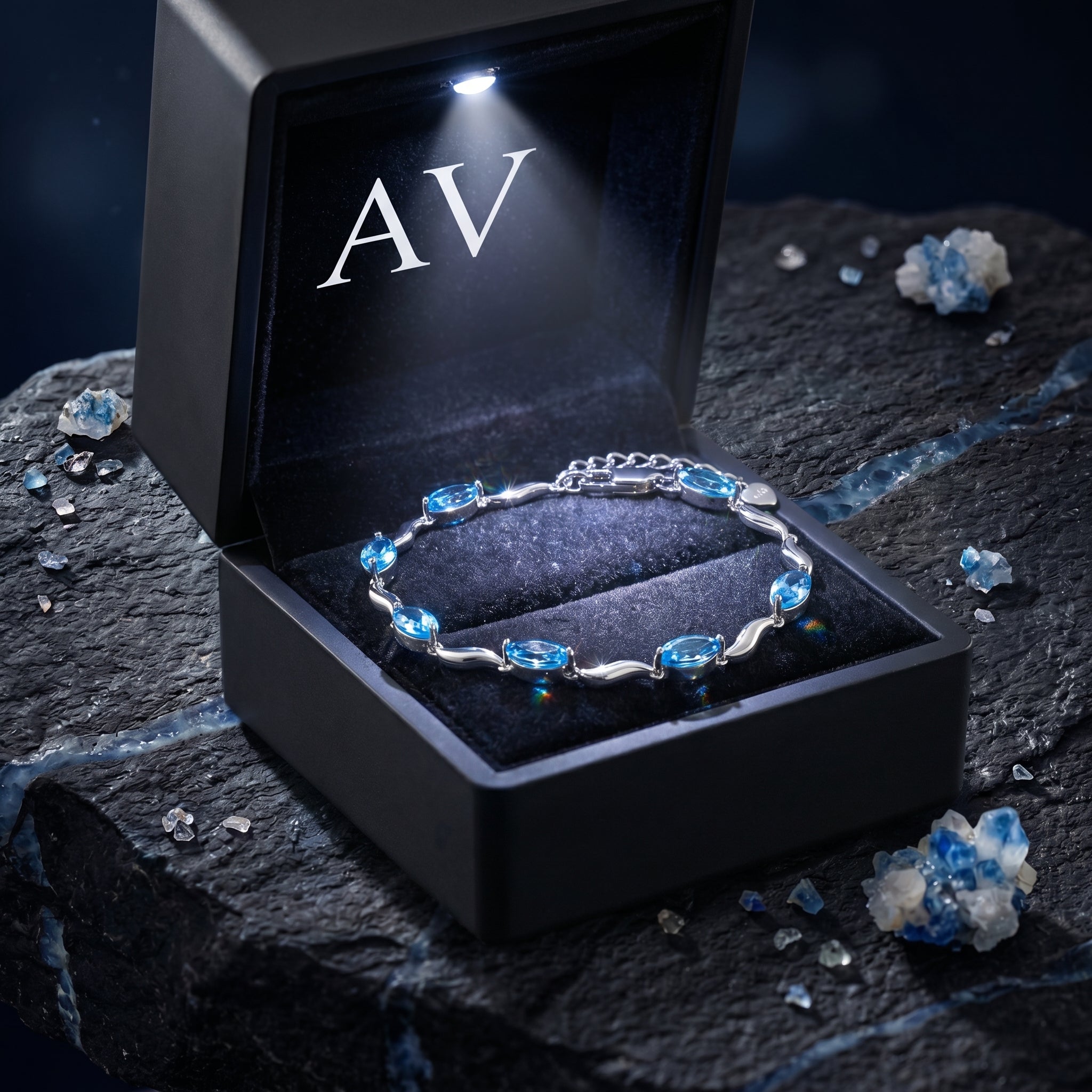 Silver marquise natural blue topaz bracelet inside a black LED-lit gift box with AV logo on a dark rock.