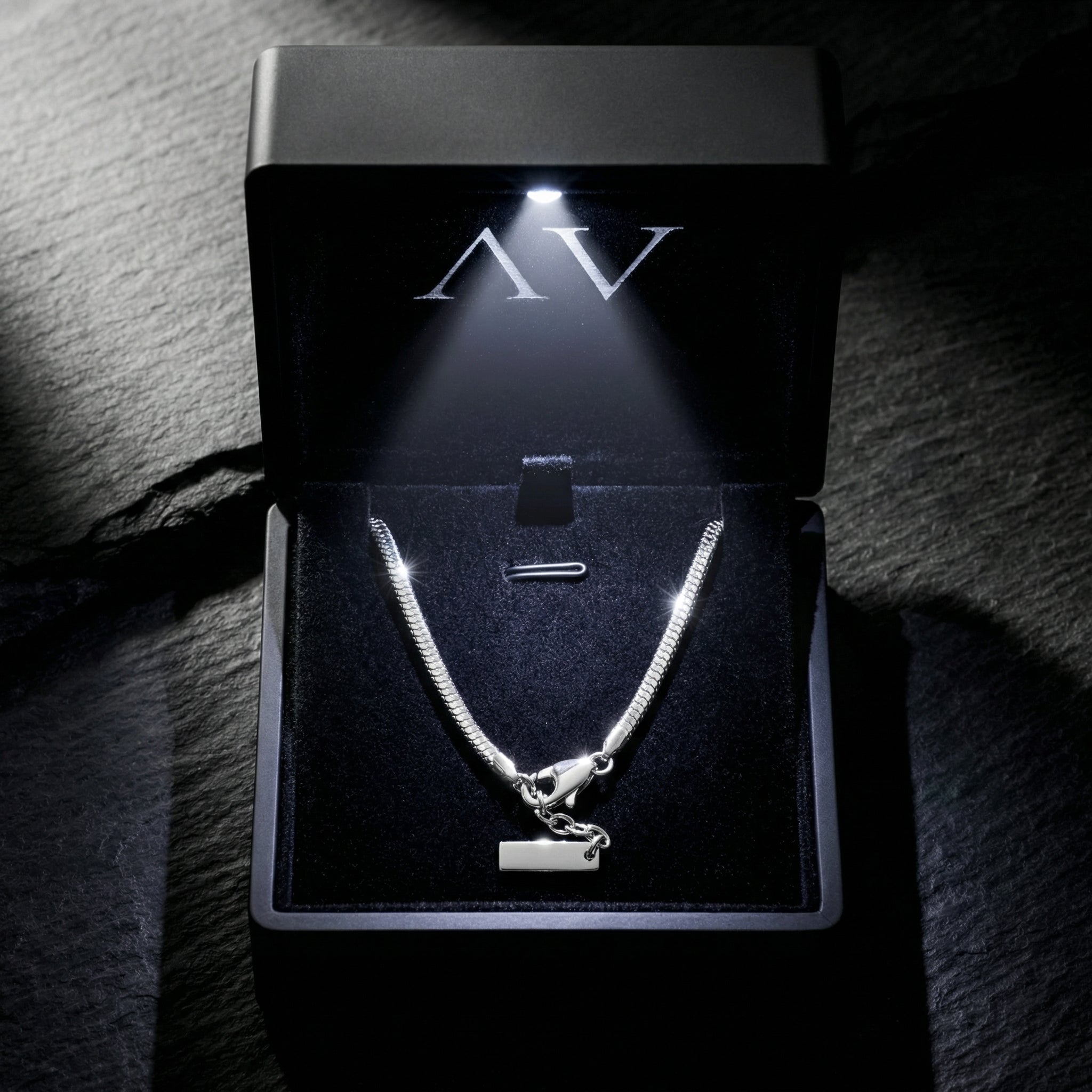 Silver stainless steel square link bracelet inside a black illuminated jewelry gift box.