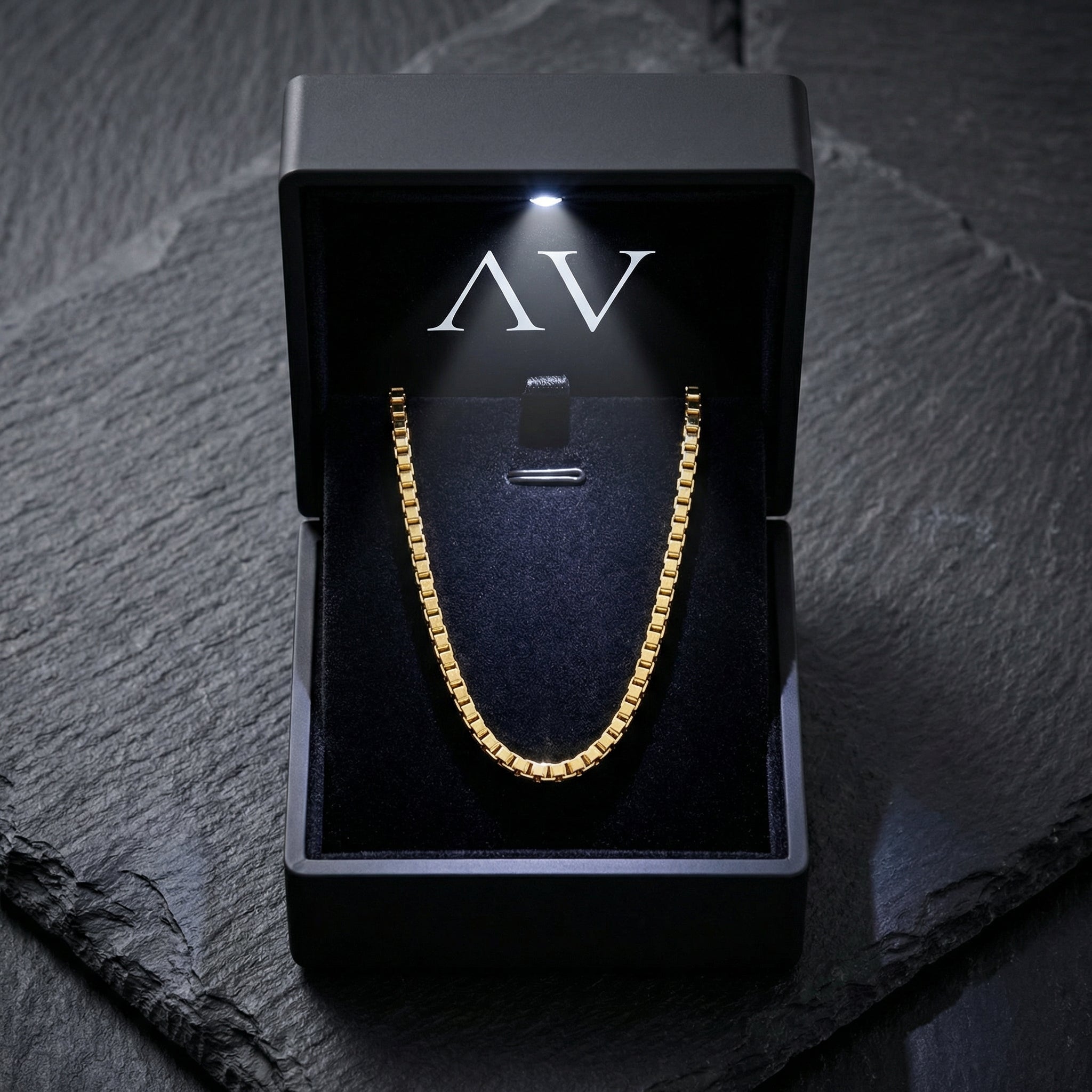 Gold Boxed In box chain necklace presented in a black LED-lit gift box on a dark stone background.