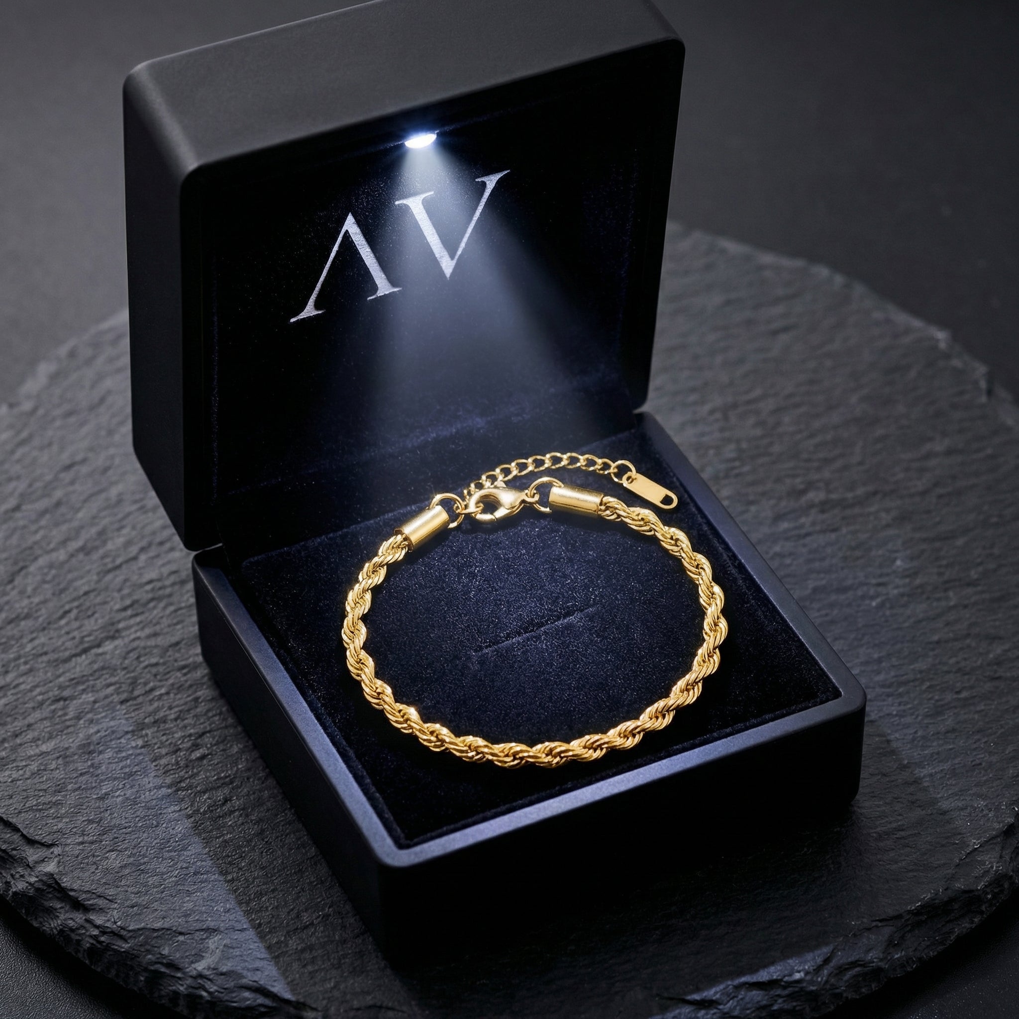 Gold rope bracelet presented in a premium black LED-lit jewelry gift box on a stone surface.