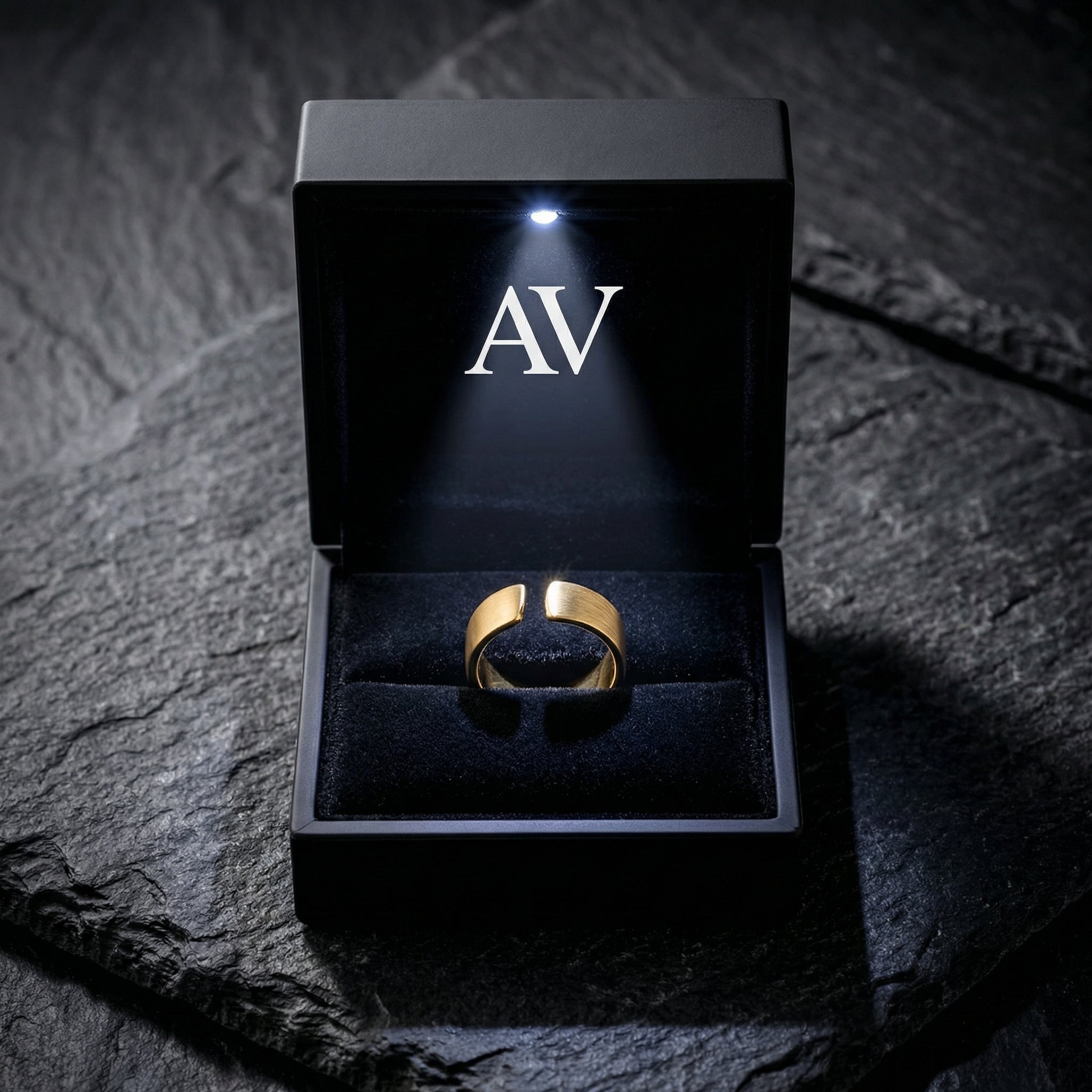 Gold stainless steel gap ring inside a black LED-lighted presentation box on a stone surface.