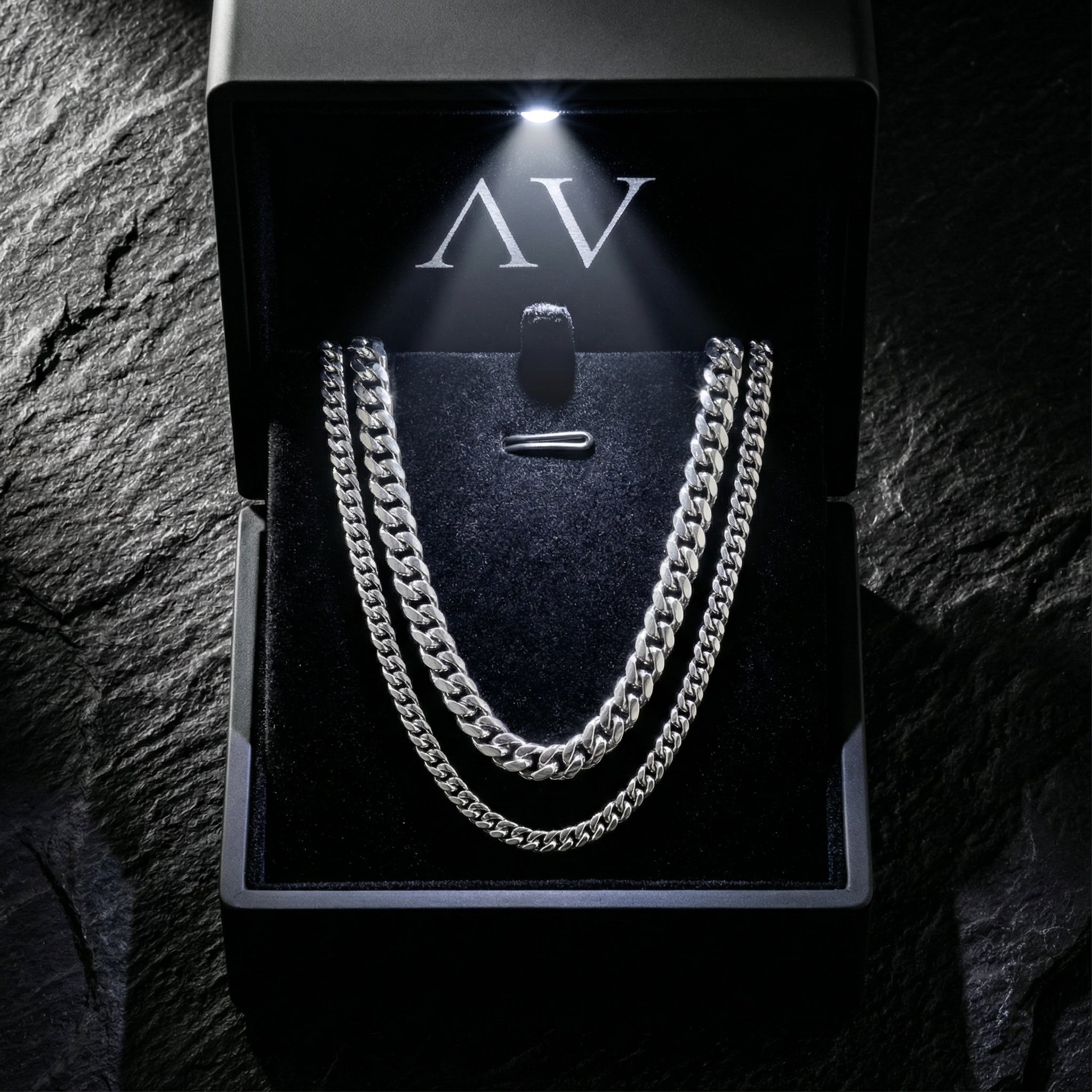 Polished silver stainless steel Cuban link necklace set inside a premium lighted gift box on a dark stone surface.