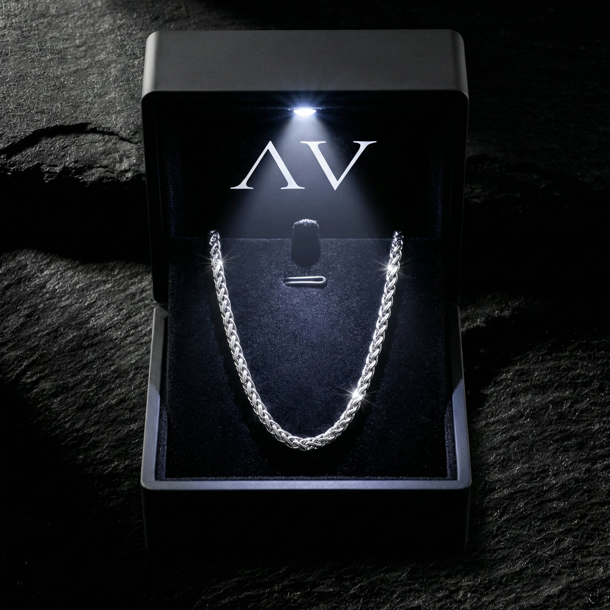 Silver stainless steel wheat chain presented in a black LED-lighted gift box on a dark stone surface.