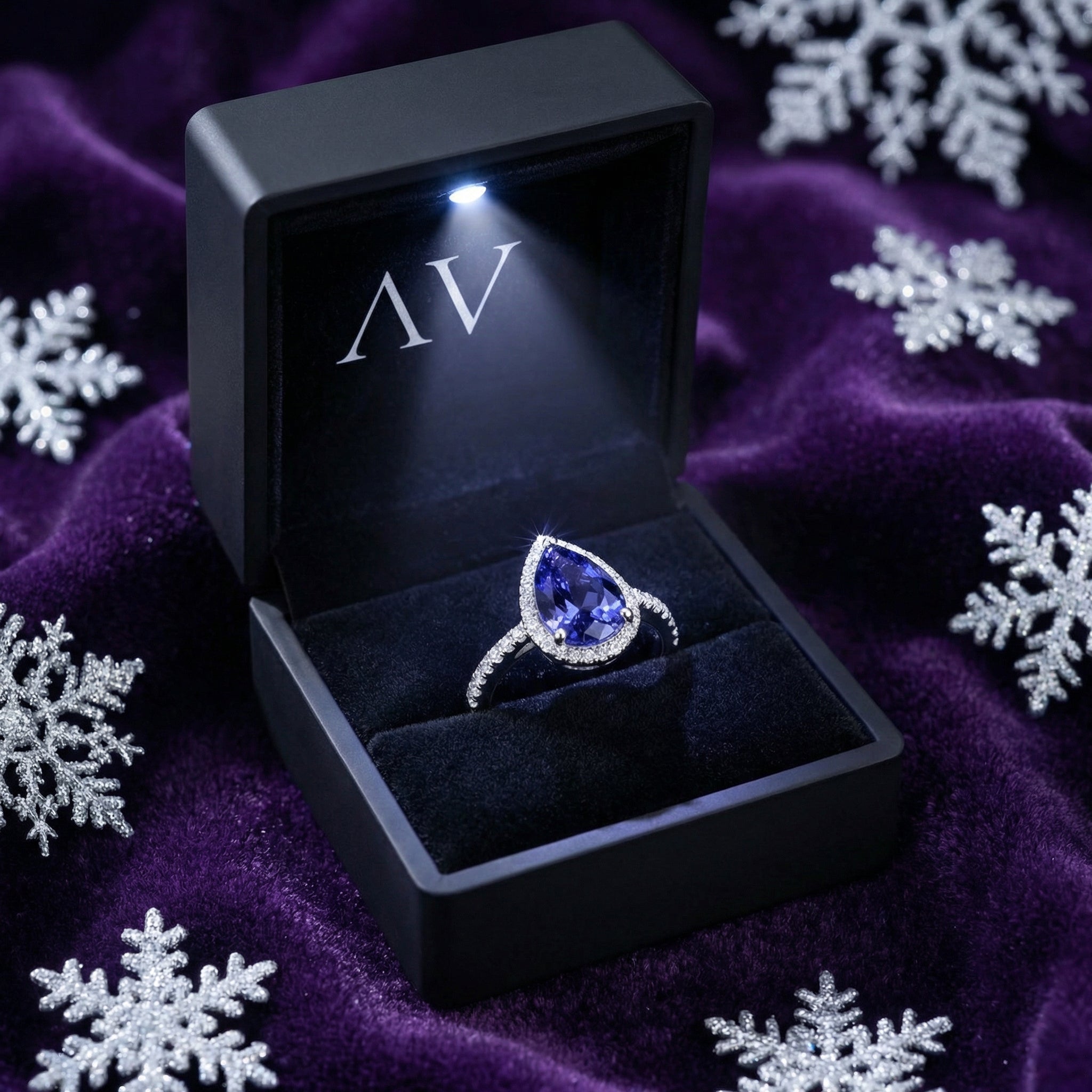 Pear cut simulated tanzanite ring presented in a lighted black jewelry box on purple velvet with snowflakes.