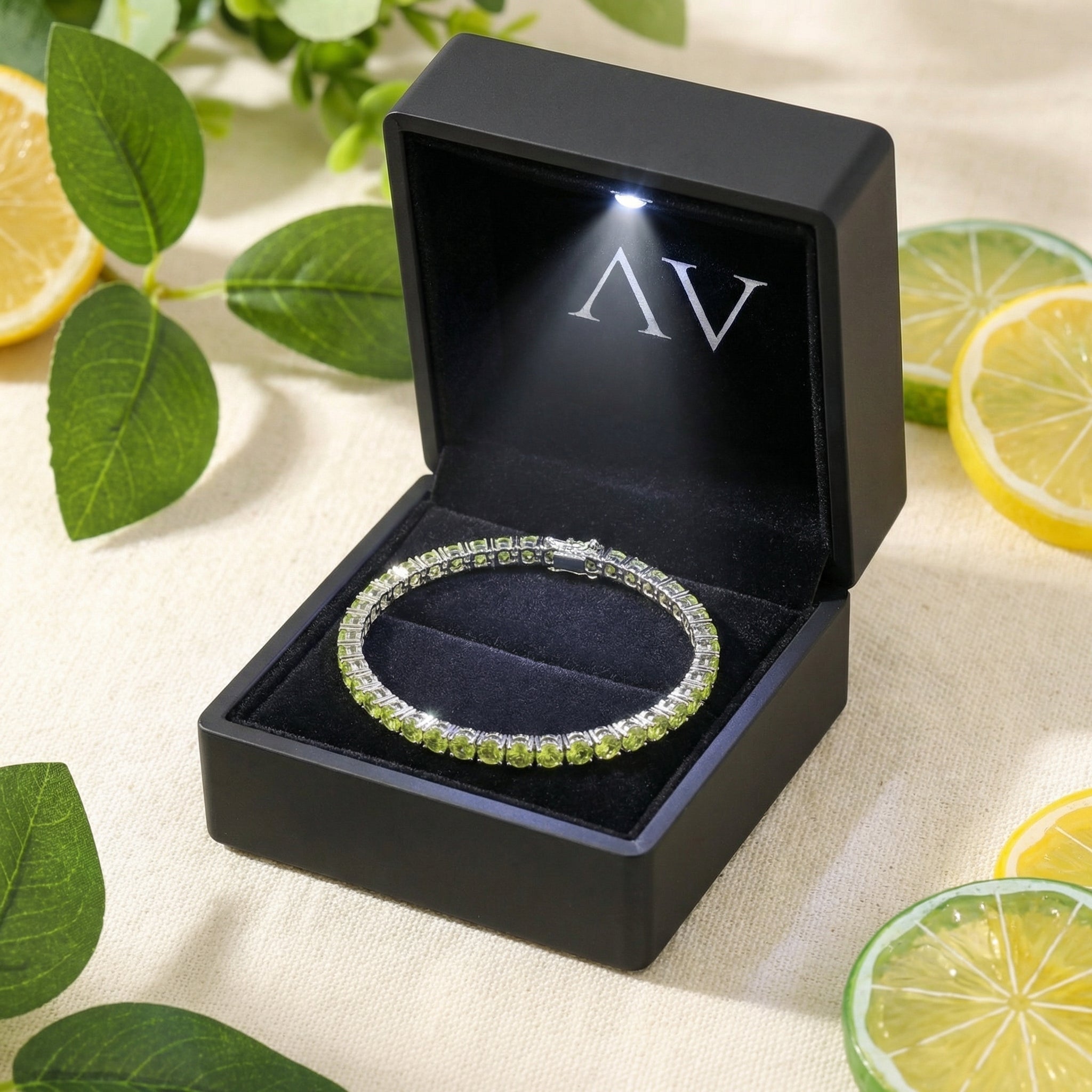 Stainless steel peridot tennis bracelet displayed in a black LED-lit gift box with citrus and leaves in background.