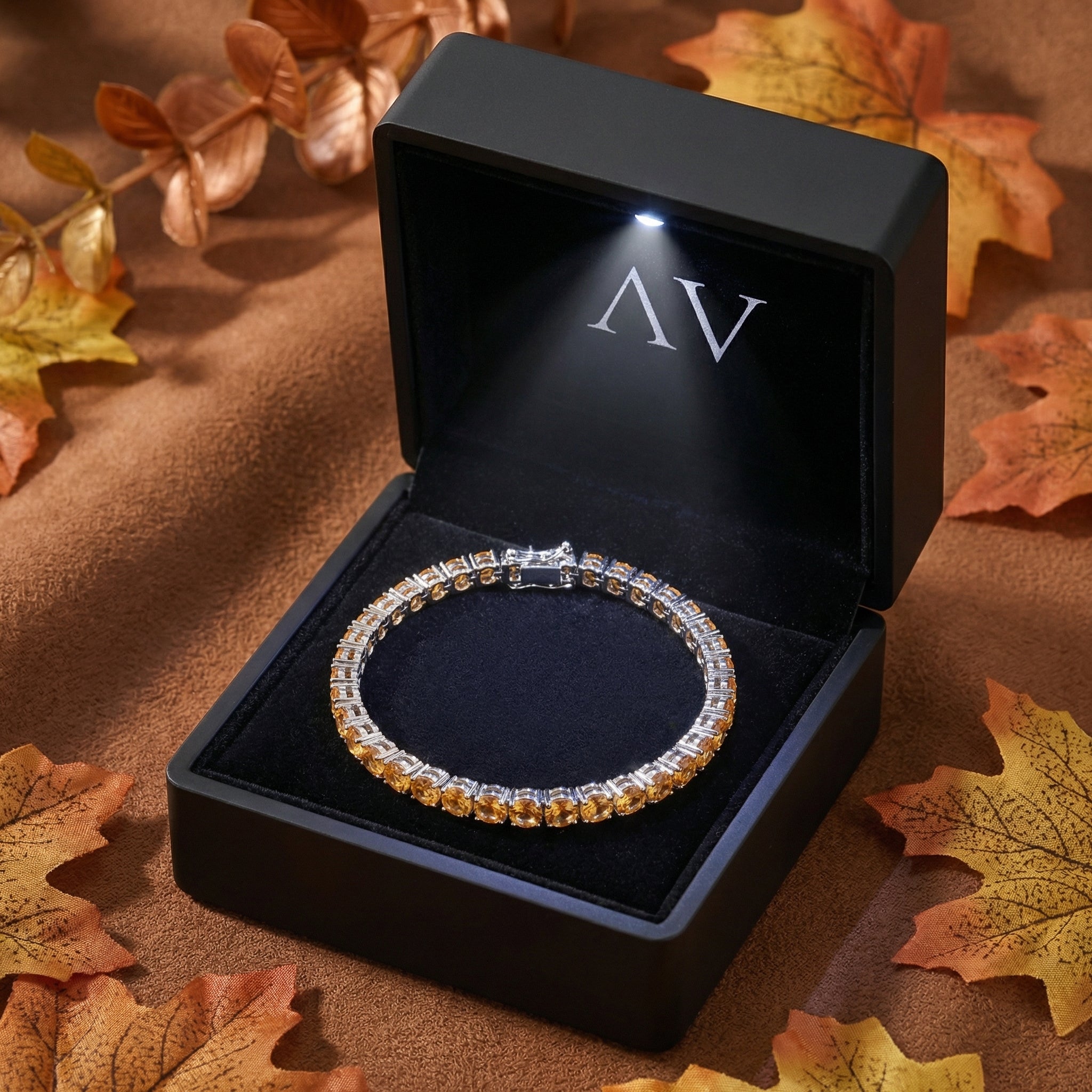 Stainless steel simulated honey topaz tennis bracelet in a lighted black AV branded gift box with autumn leaves.
