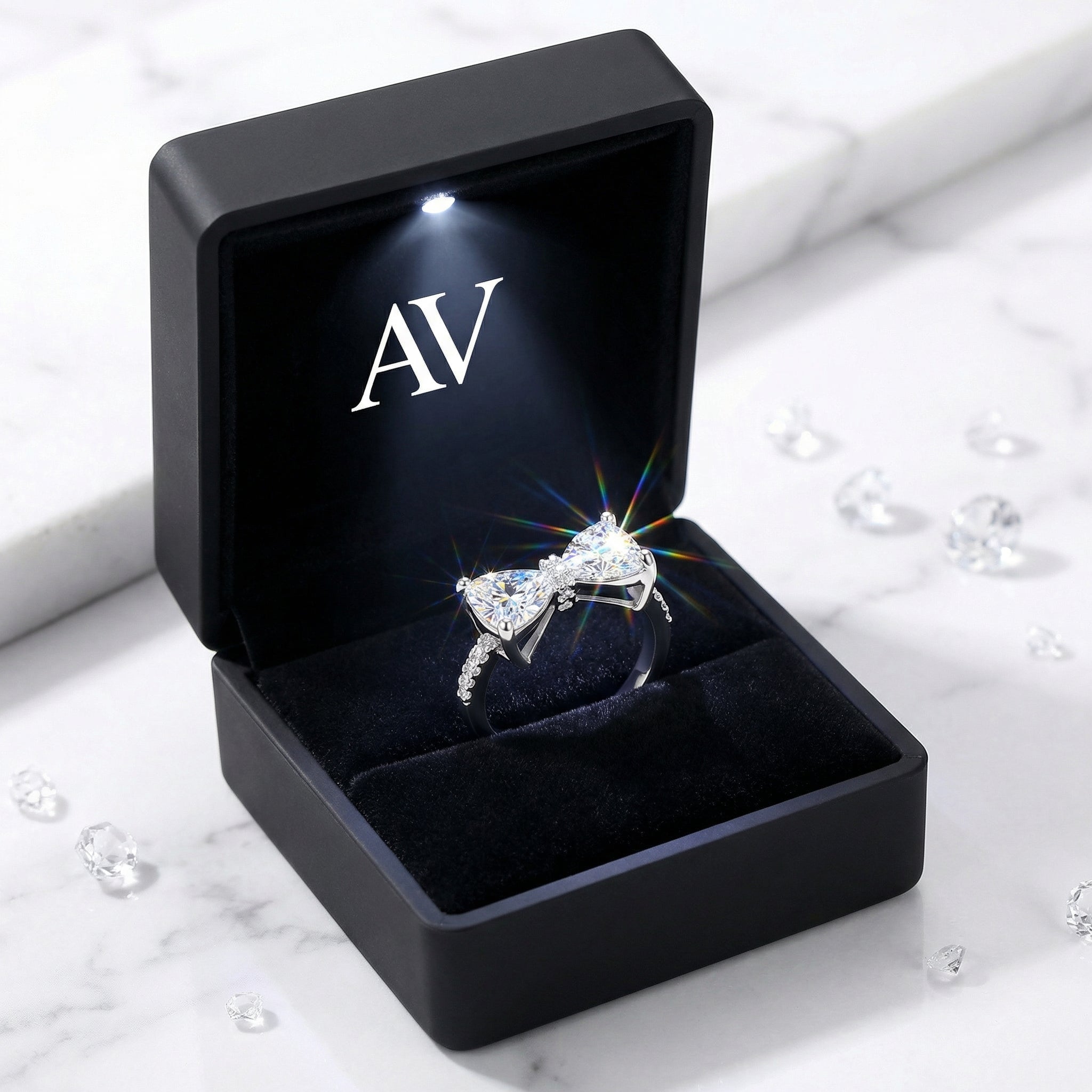 Lysandra bow ring in a black LED-lit jewelry gift box on a marble surface with loose stones.