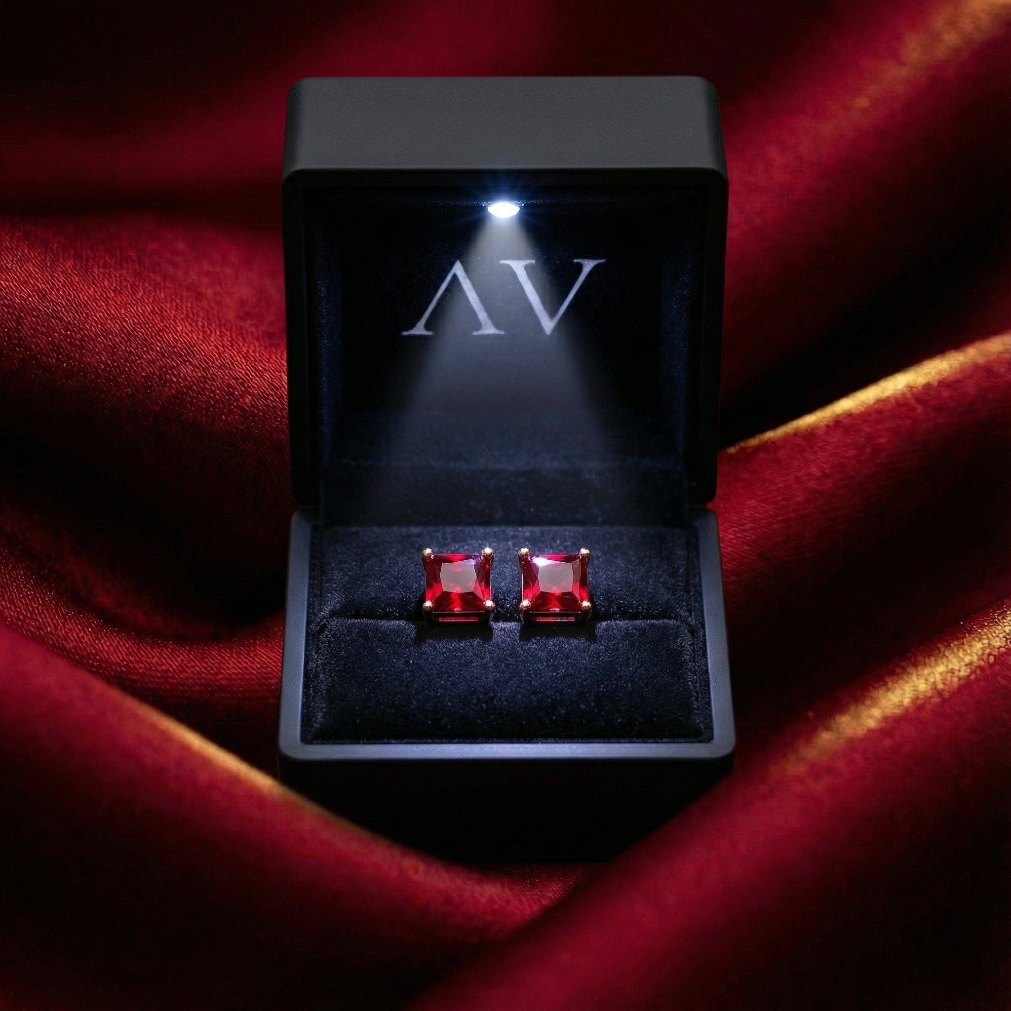 Square simulated ruby stud earrings inside a black LED-lighted jewelry box on red fabric.