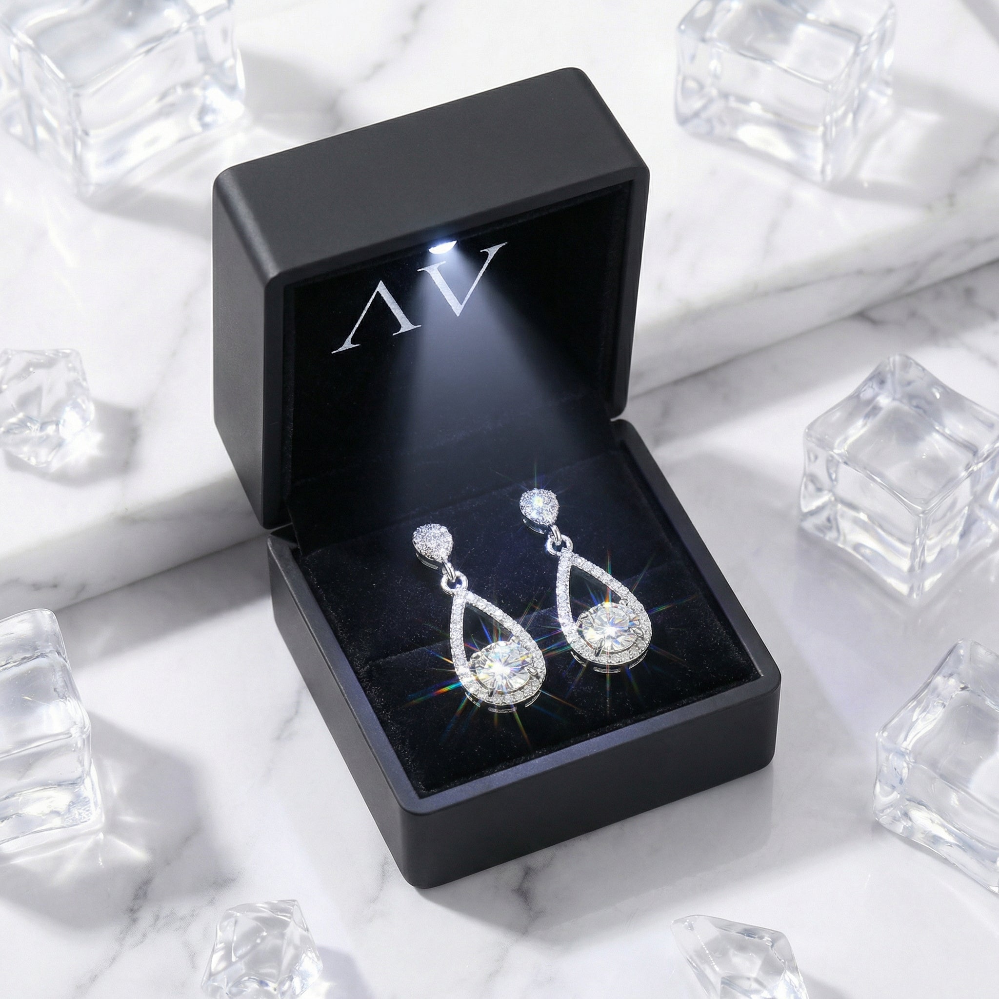 Sterling silver teardrop zirconia earrings presented in a black LED-lit gift box on a marble background.