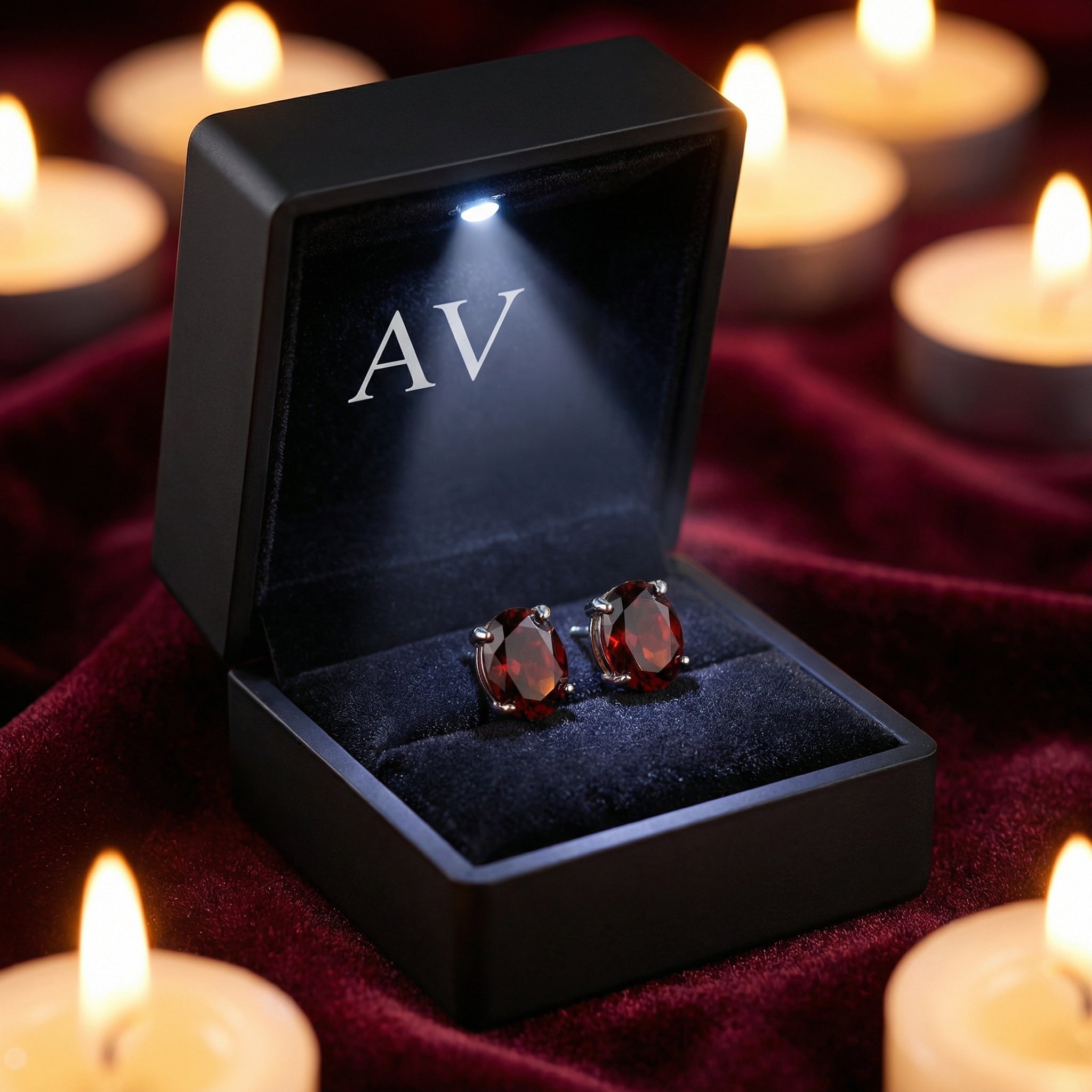 Oval cut simulated garnet earrings in a black LED-lit gift box surrounded by warm candlelight.