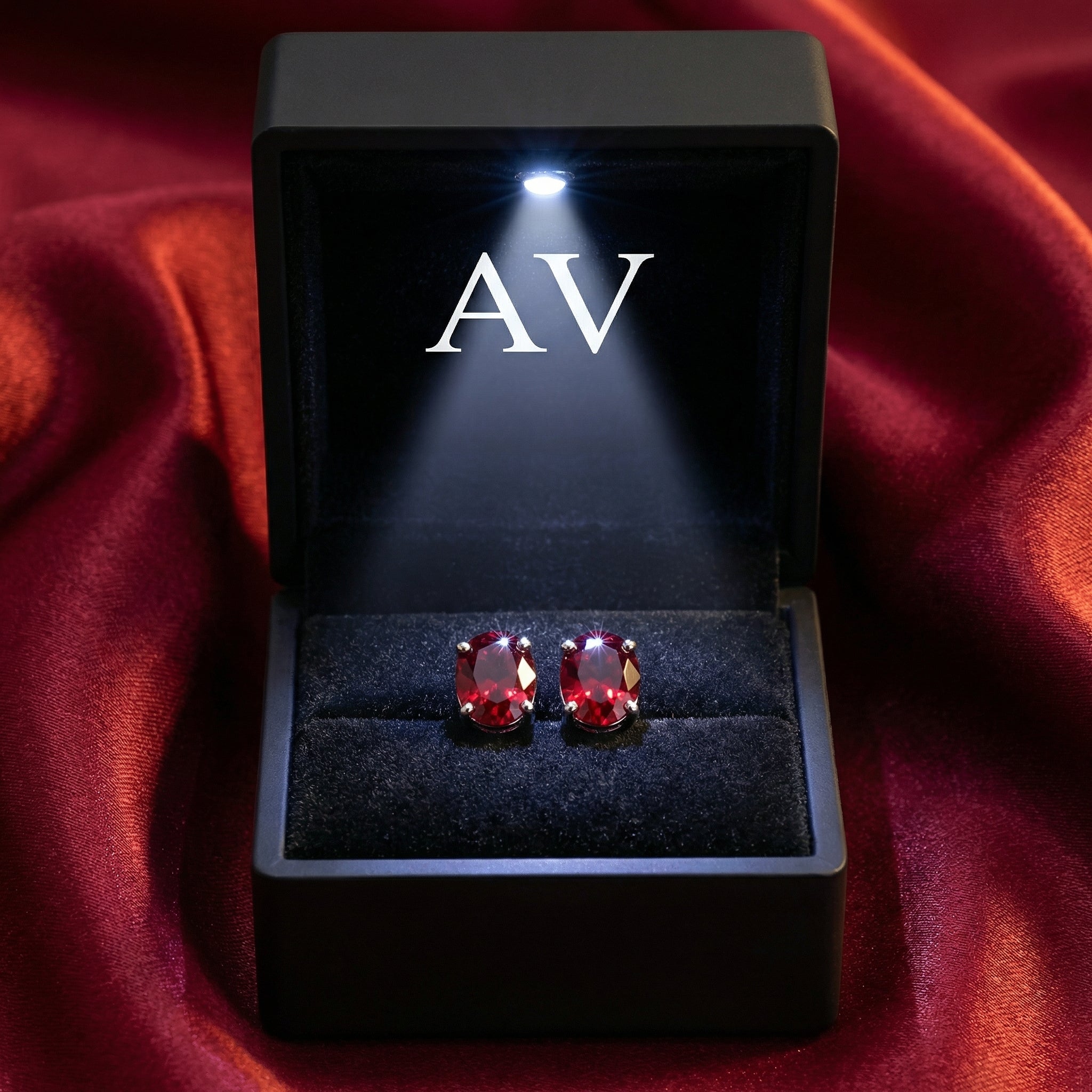 Oval-cut simulated ruby stud earrings in sterling silver inside a lighted black jewelry box.