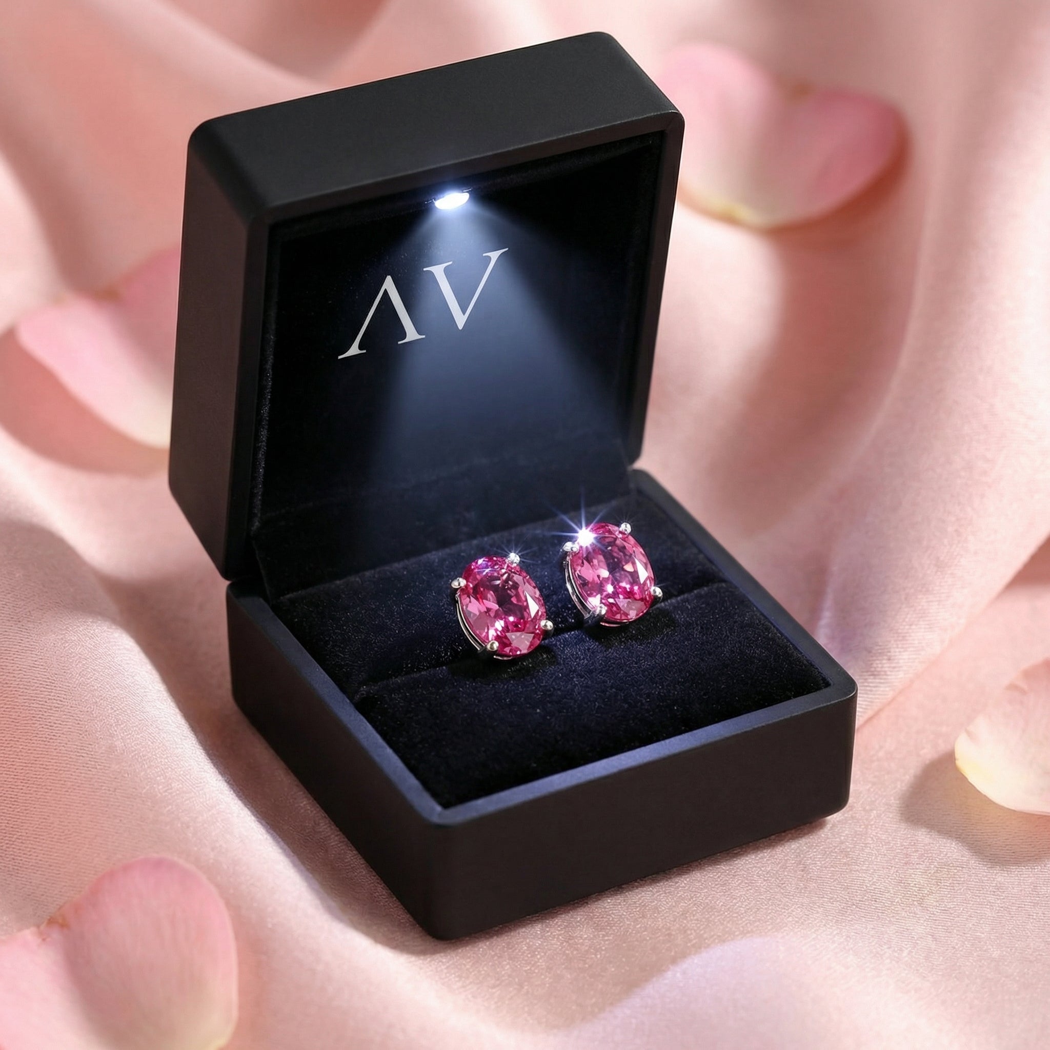 Oval cut simulated pink tourmaline silver studs in a black LED-lit jewelry box on pink satin fabric.