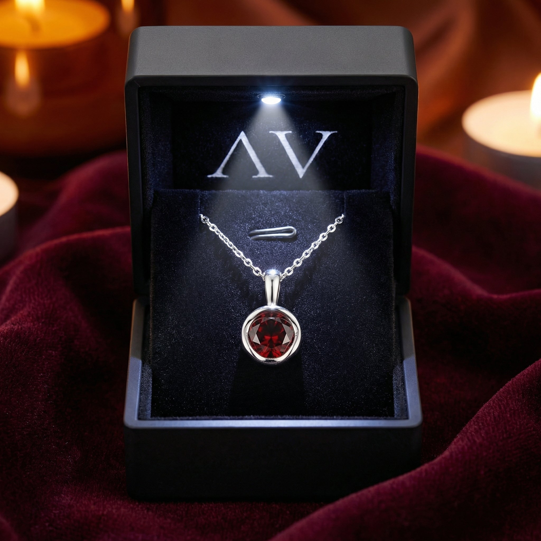 Round cut red garnet sterling silver pendant in a black LED-lit gift box, presented on red velvet fabric.