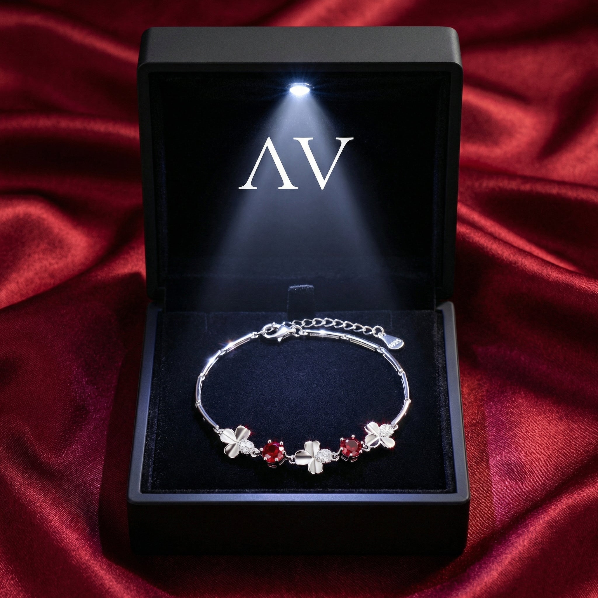 Silver clover bracelet with red simulated rubies in a black LED-lit presentation box.