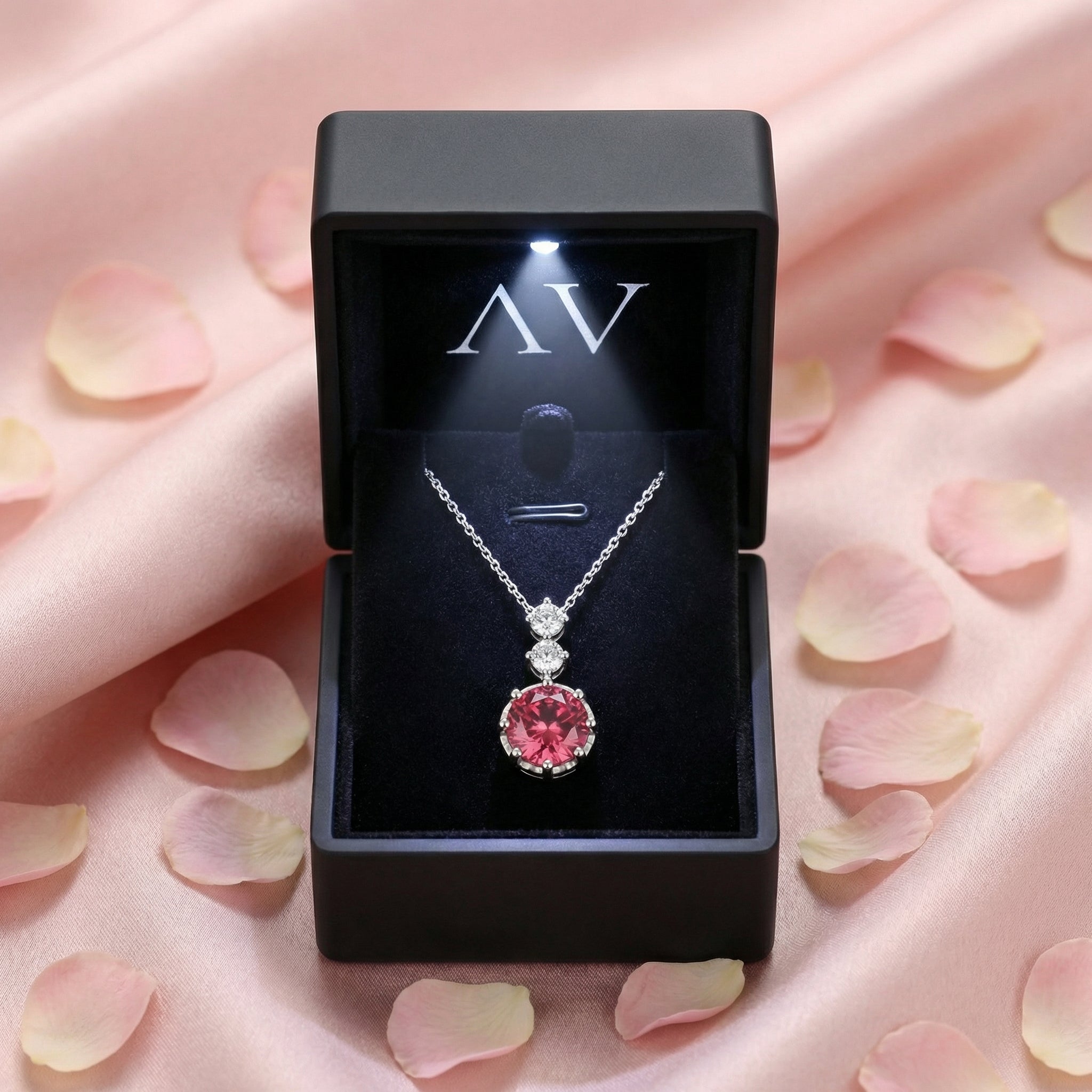 Sterling silver pink tourmaline necklace in a black LED-lit gift box on pink silk with rose petals.