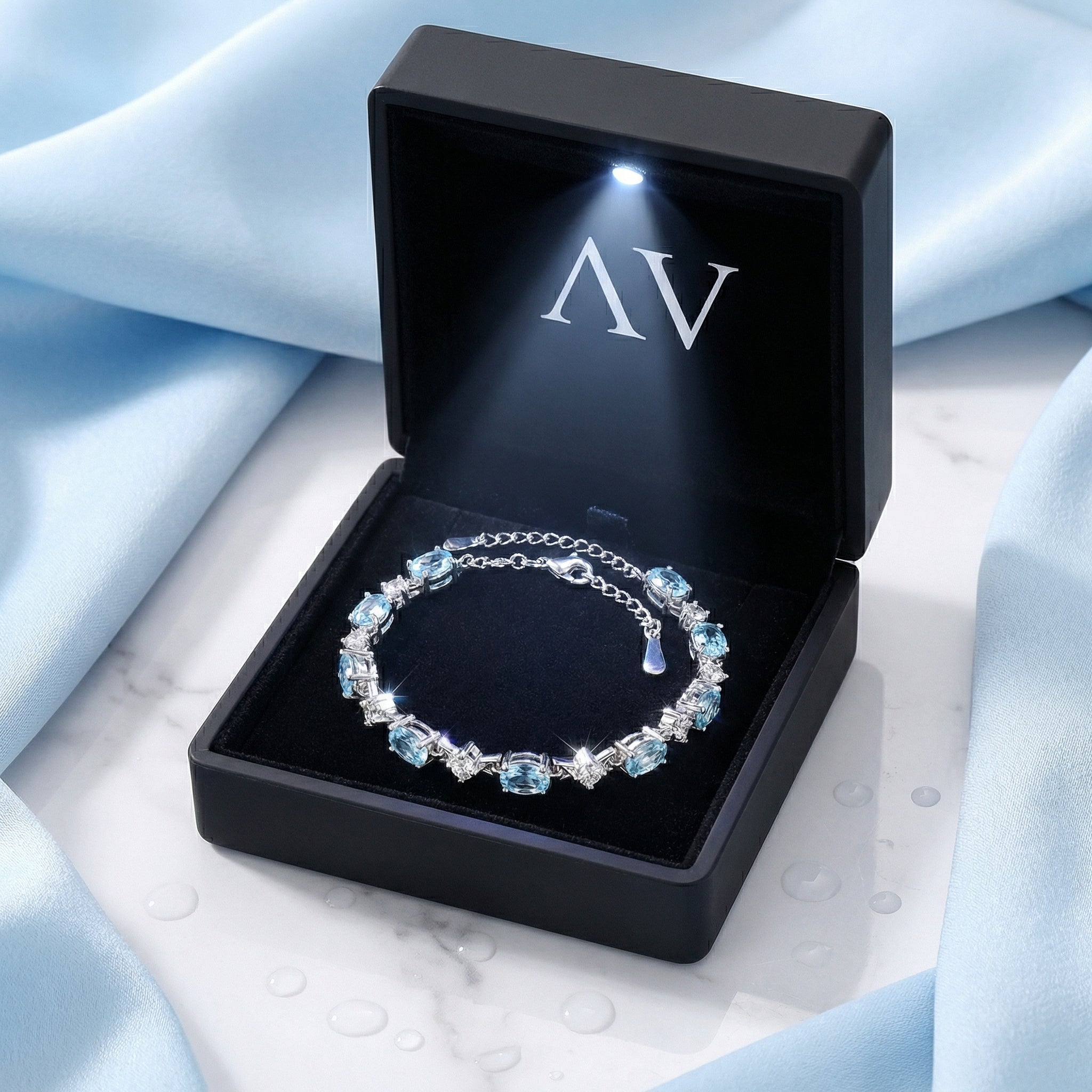 Sterling silver simulated aquamarine station bracelet presented in a black lighted jewelry gift box.