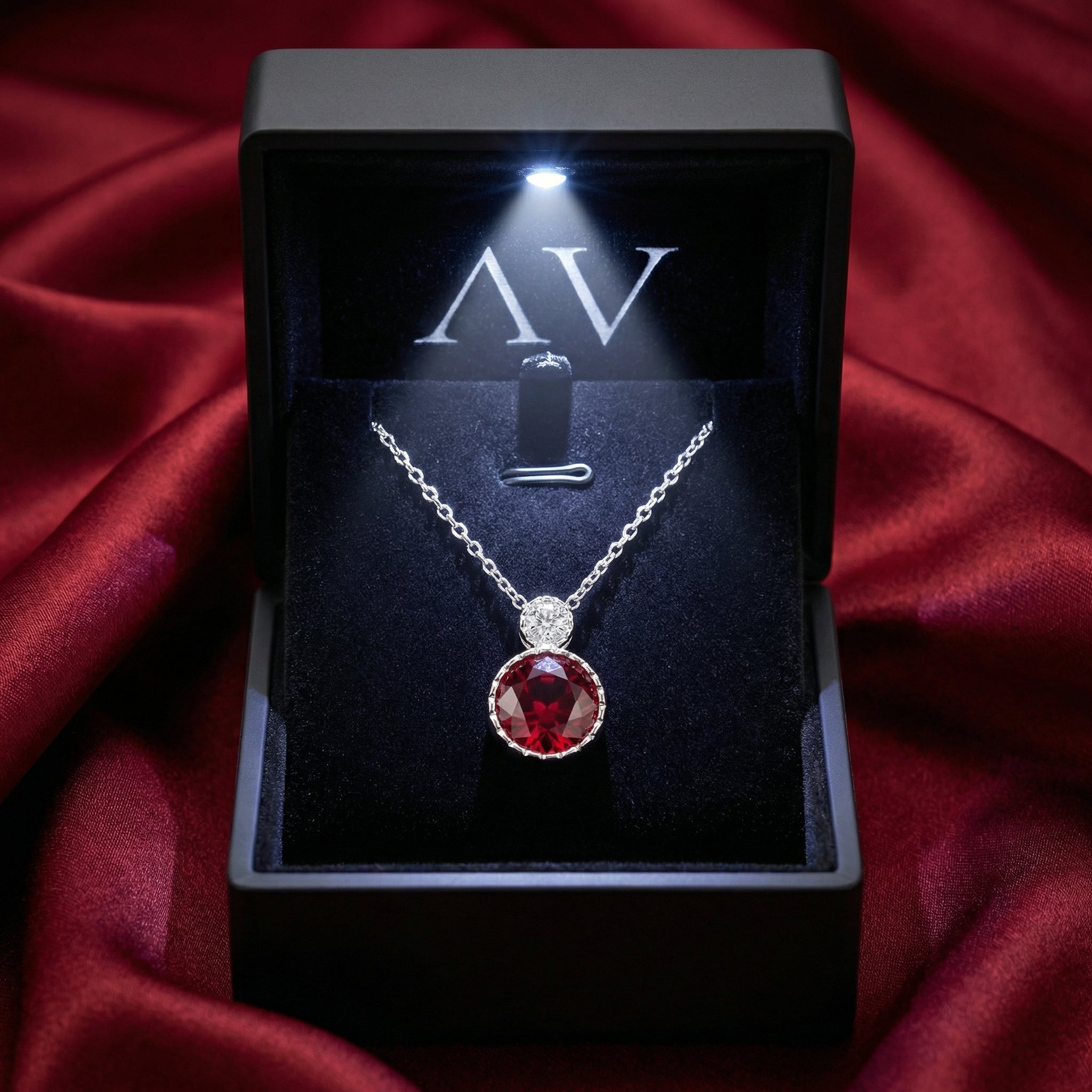 Round simulated ruby pendant in S925 sterling silver inside a lighted black gift box on red satin.