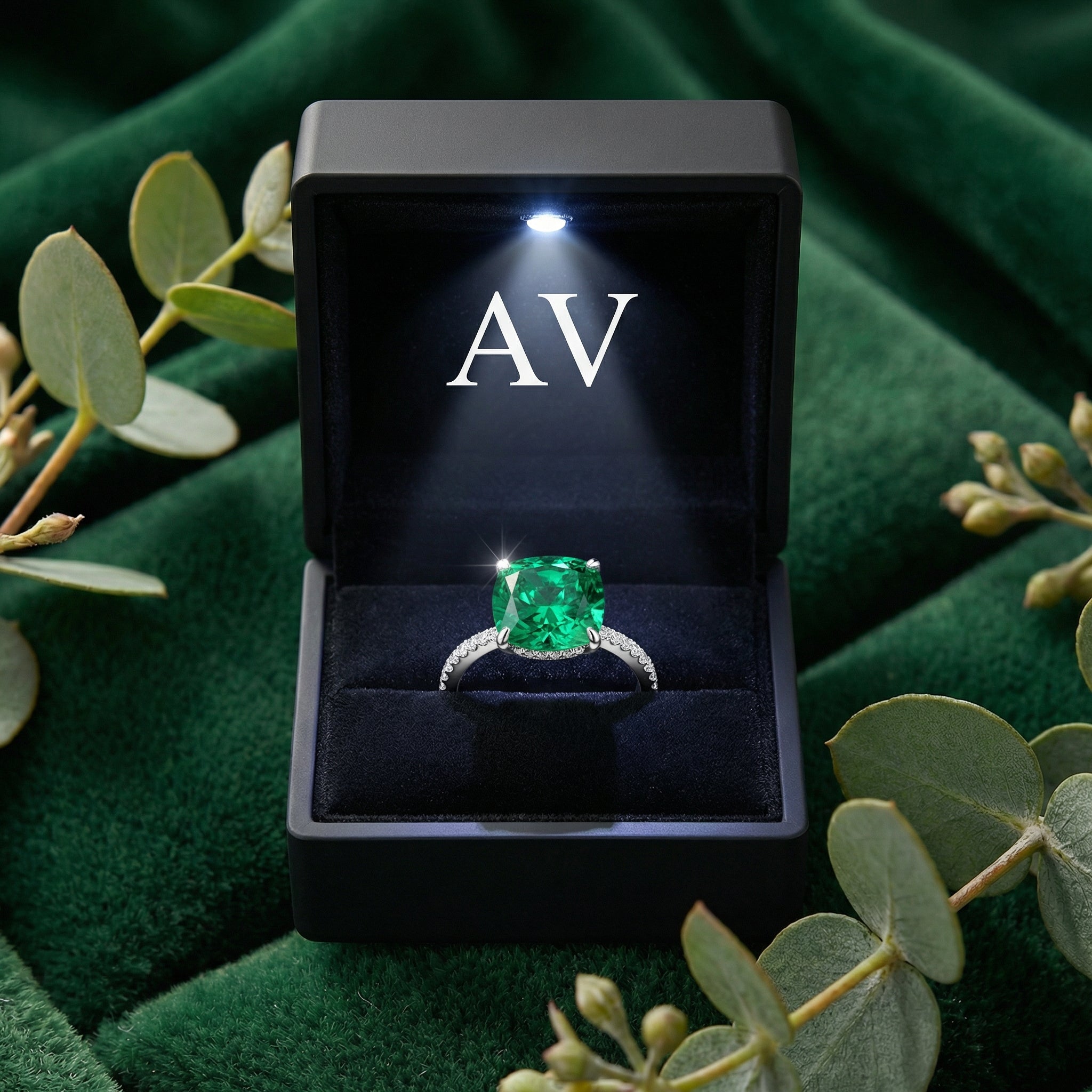 Cushion-cut simulated emerald ring in S925 sterling silver inside a black LED-lit jewelry box with AV logo.