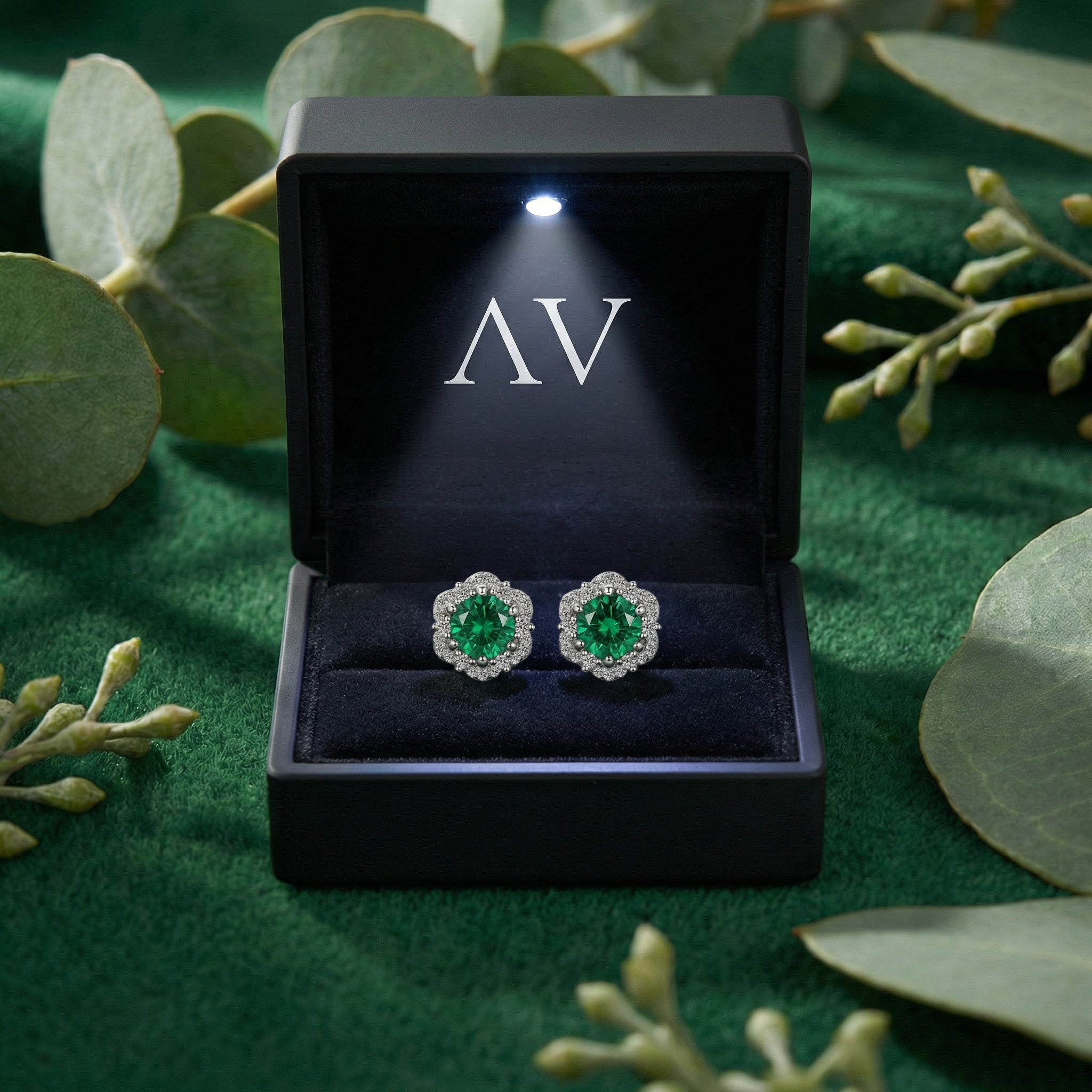 Sterling silver simulated emerald halo stud earrings in a black LED-lit jewelry gift box.