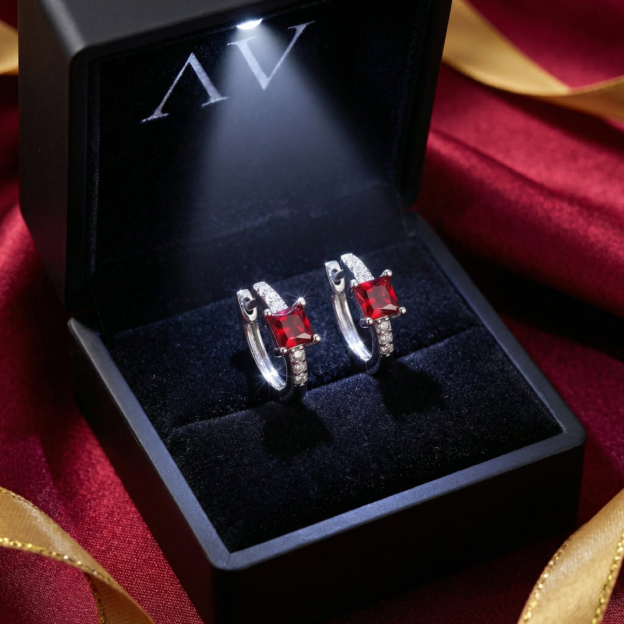 Pair of silver square ruby huggies in a lighted black jewelry presentation box on red silk.
