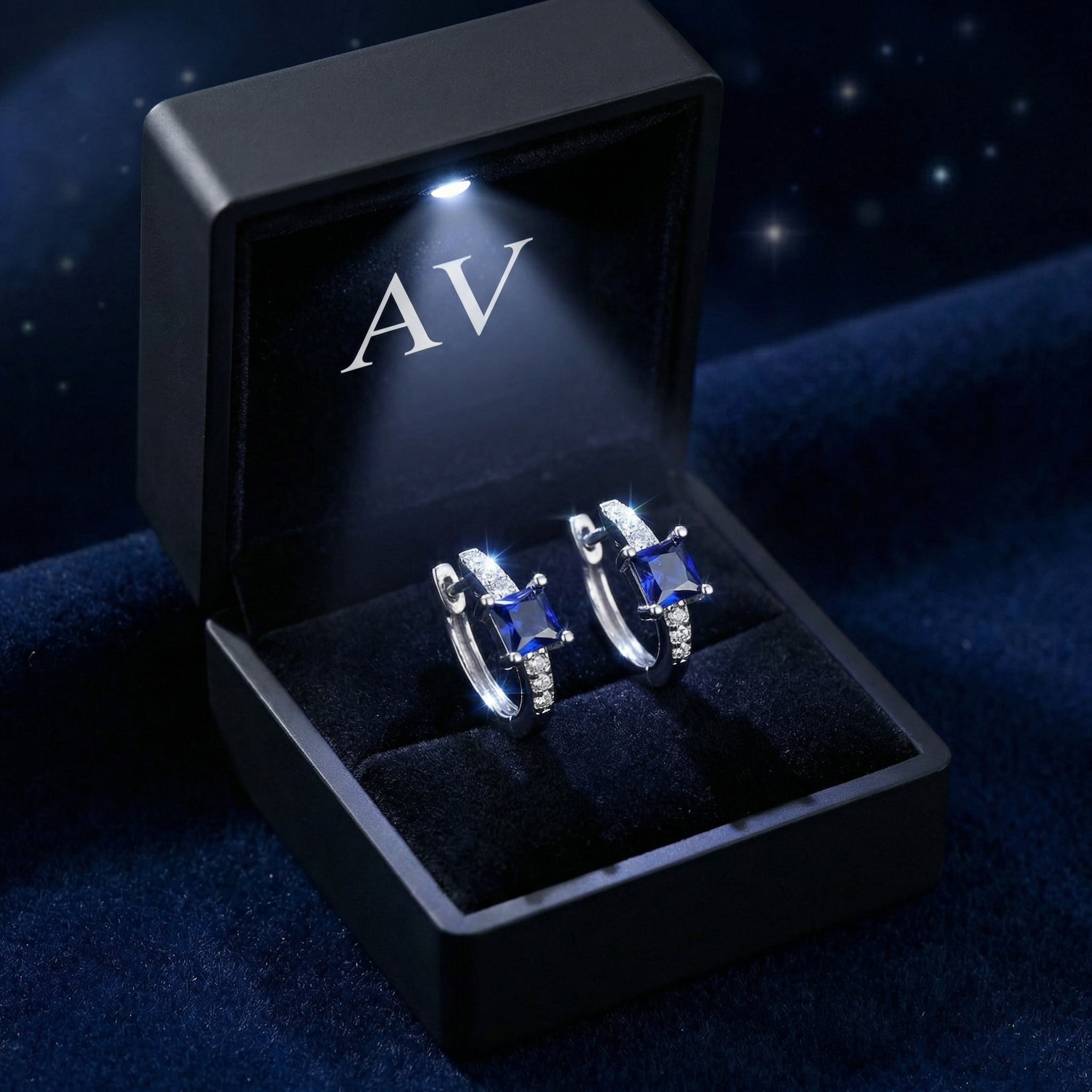 Pair of square-cut simulated sapphire sterling silver huggie earrings in a black LED-lit jewelry box.