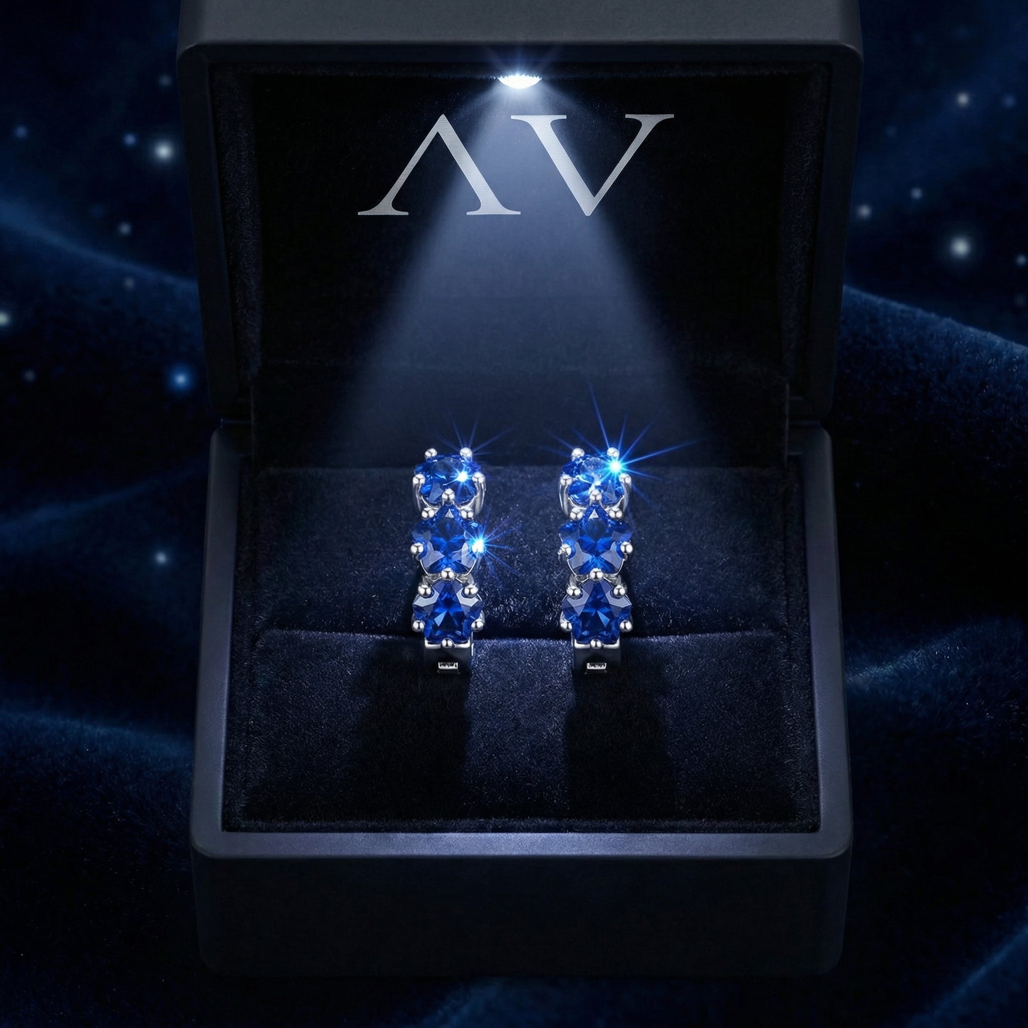 Sterling silver star huggie earrings with blue sapphires inside a lighted black AV branded jewelry box.