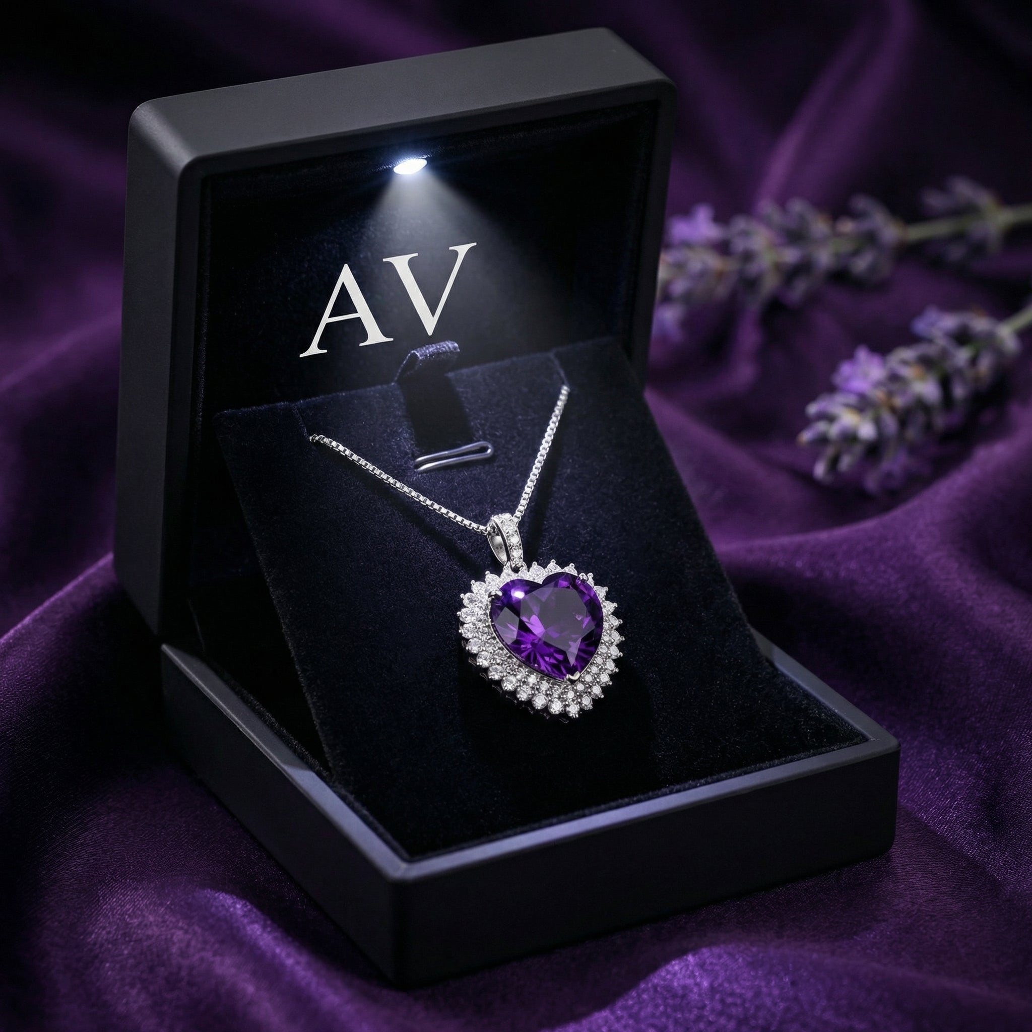 Heart-cut amethyst pendant in a silver halo setting inside a lighted black jewelry gift box with AV branding.