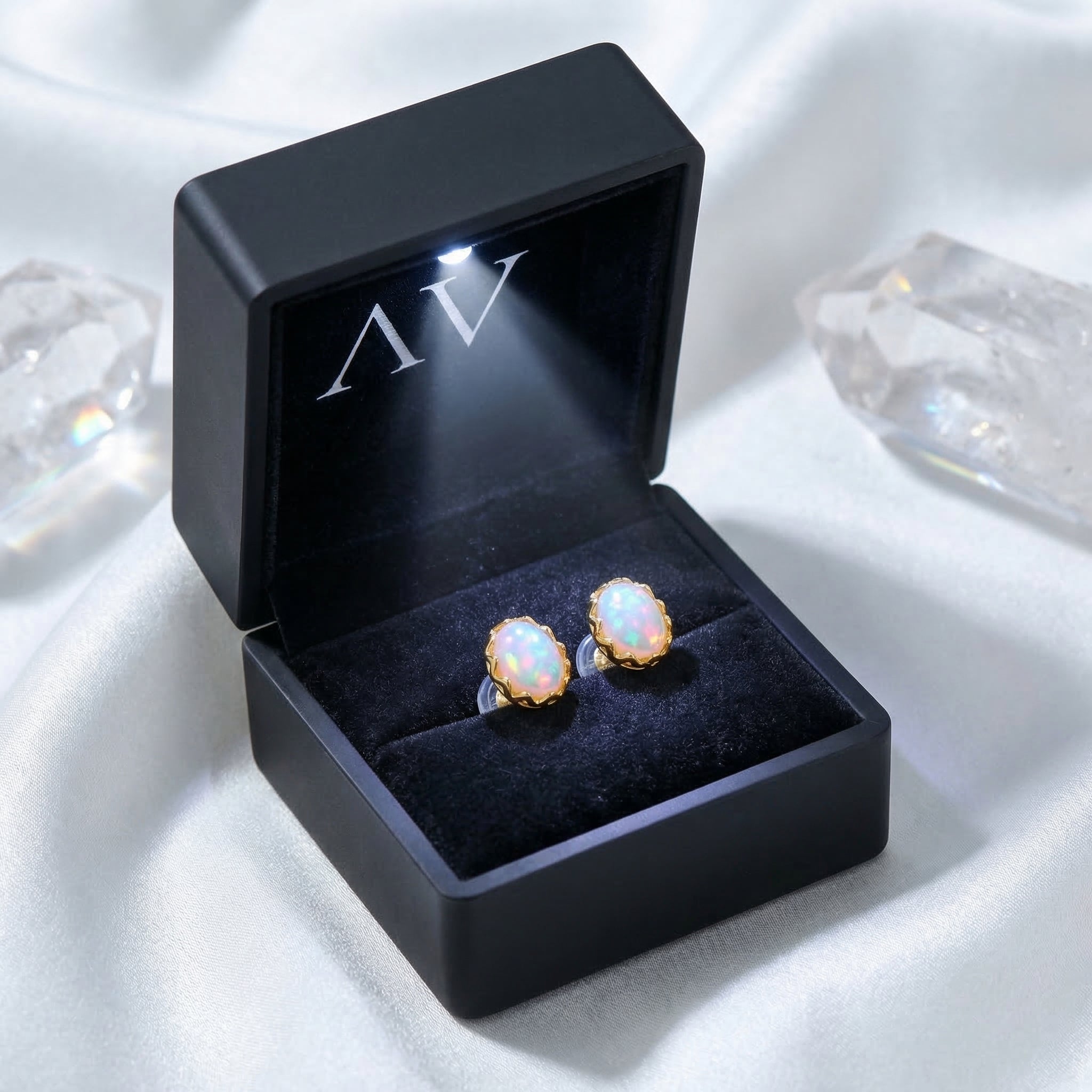 Yellow gold Novalie oval white opal stud earrings displayed in a black illuminated jewelry gift box.