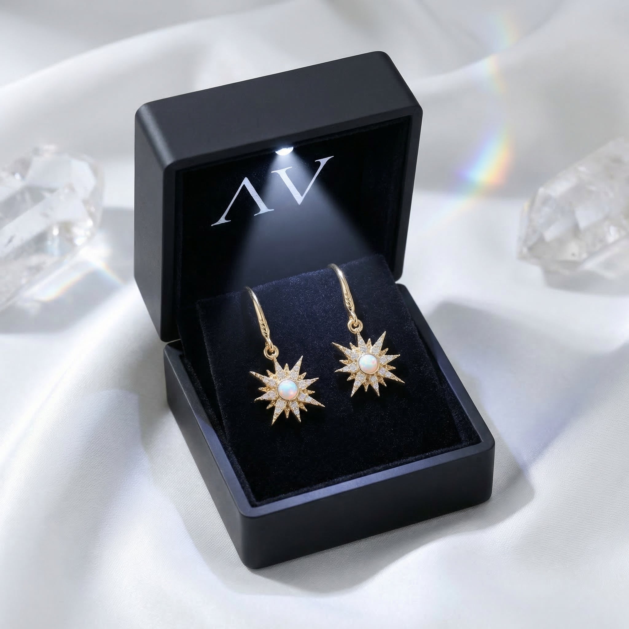 Gold-tone starburst drop earrings with round white opals displayed in a black LED-lit jewelry gift box.