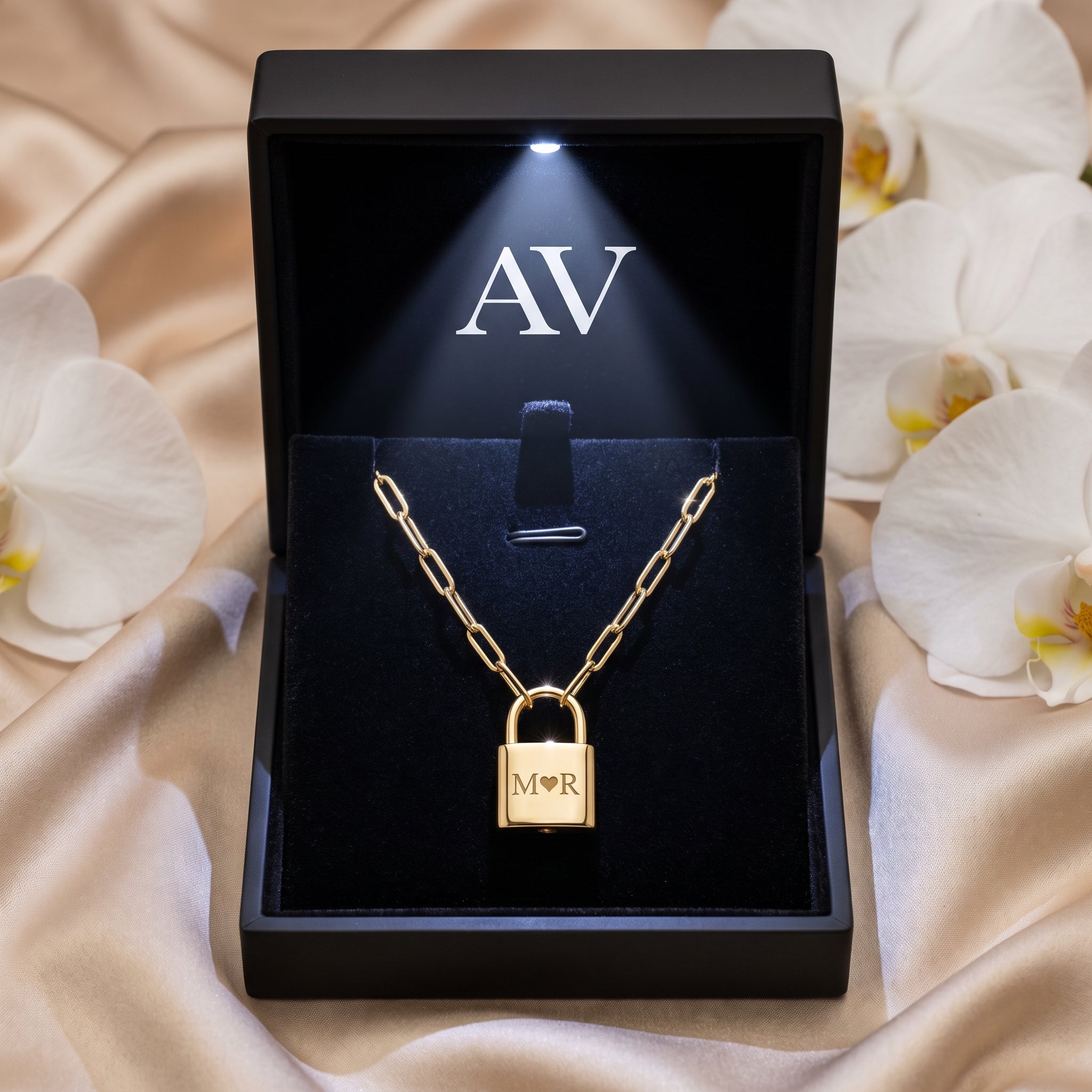 Gold padlock necklace in a black LED-lit presentation box surrounded by white orchids.