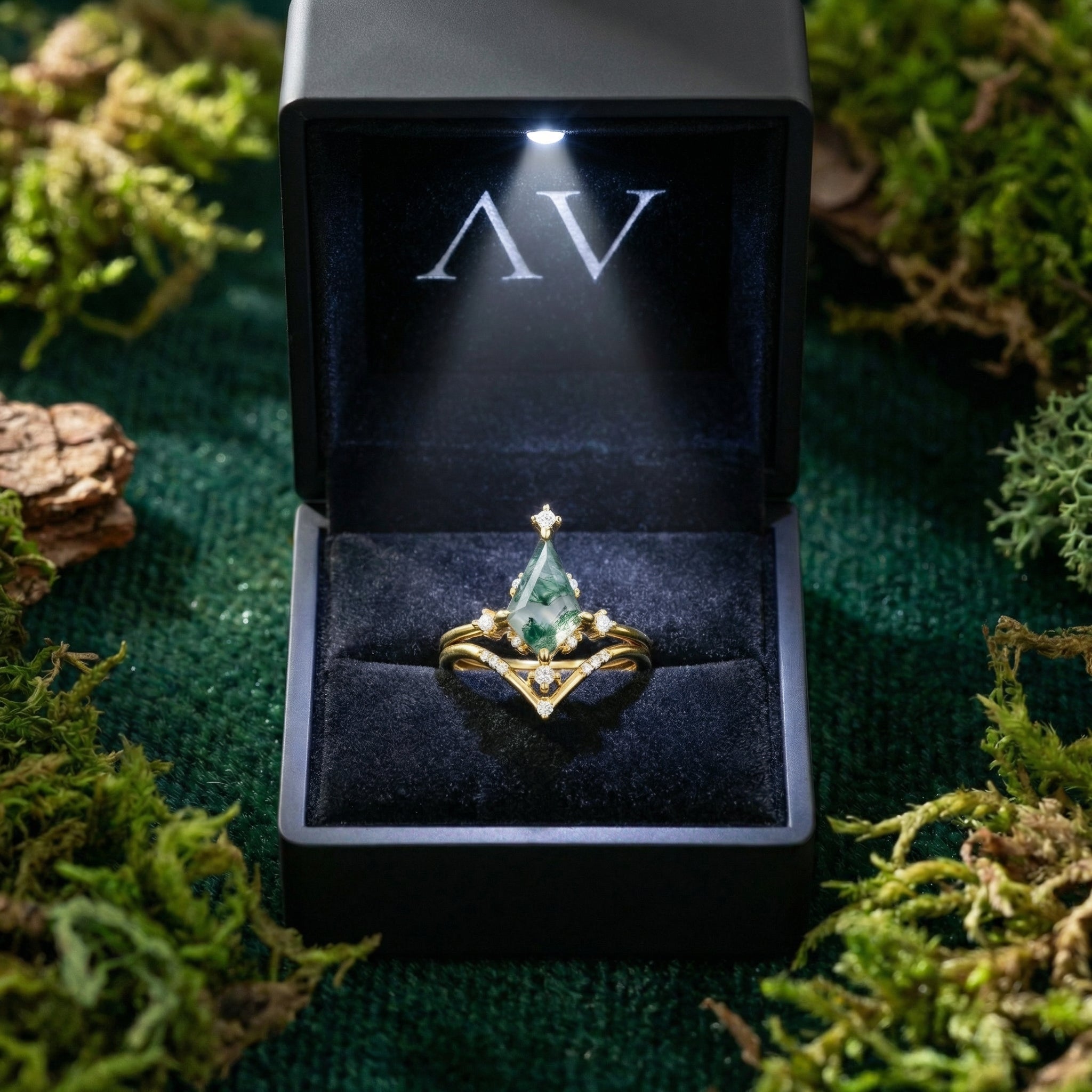 Kite cut moss agate gold ring set inside a black LED-lighted gift box on a mossy background.