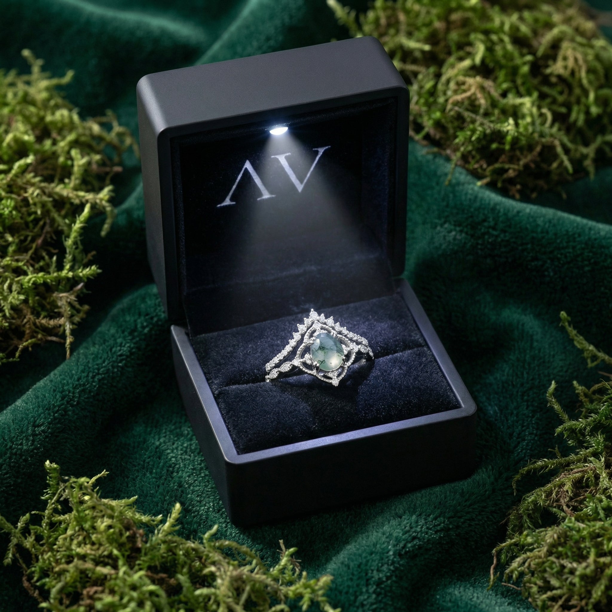 Oval cut moss agate ring set in a lighted black gift box, presented on green velvet with moss.