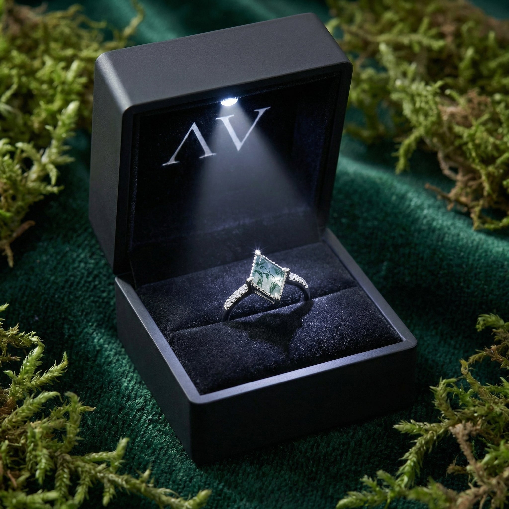 Kite cut natural moss agate ring presented in a black LED lighted gift box on a green velvet background.