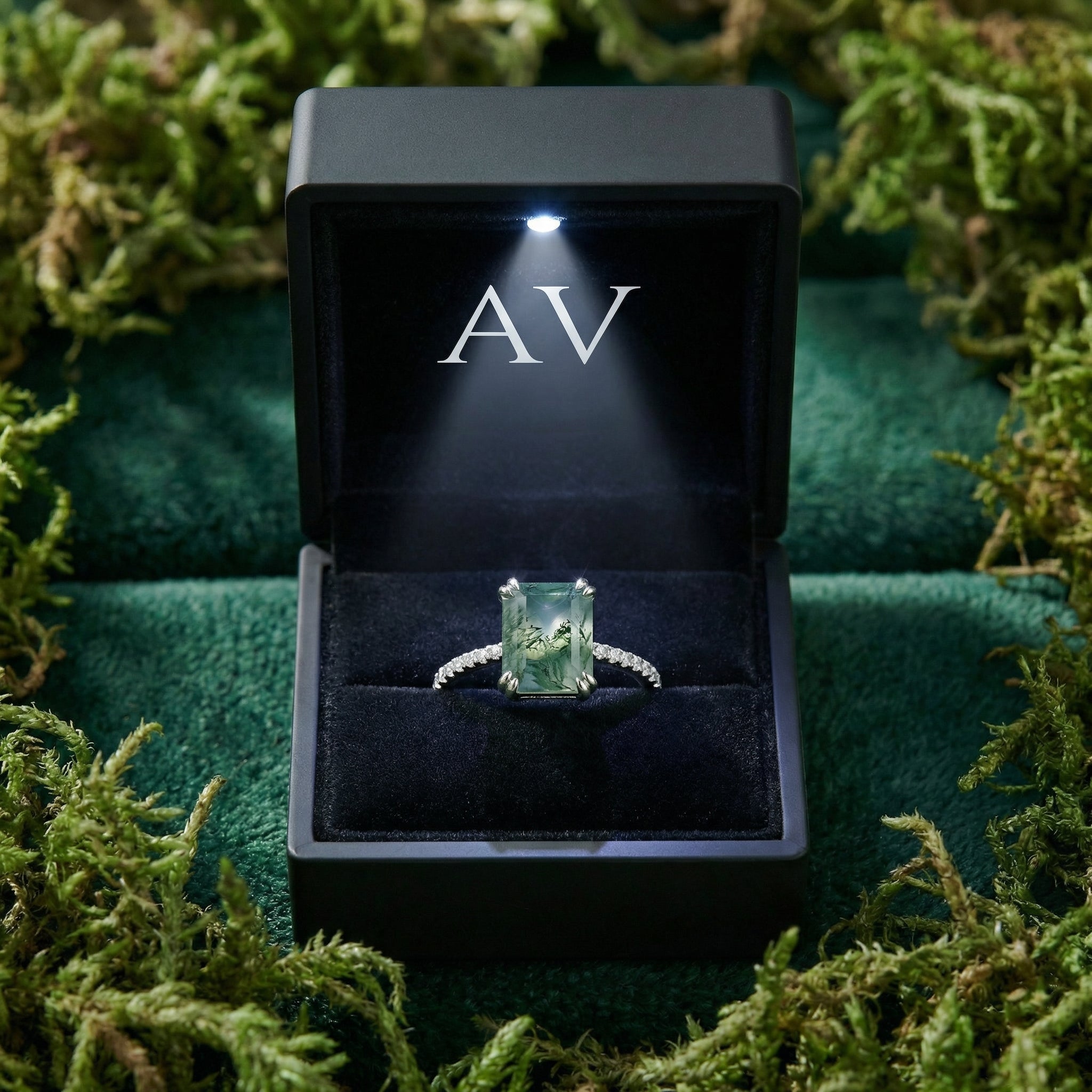 Rectangular moss agate ring in S925 sterling silver presented in a black lighted gift box surrounded by green moss.