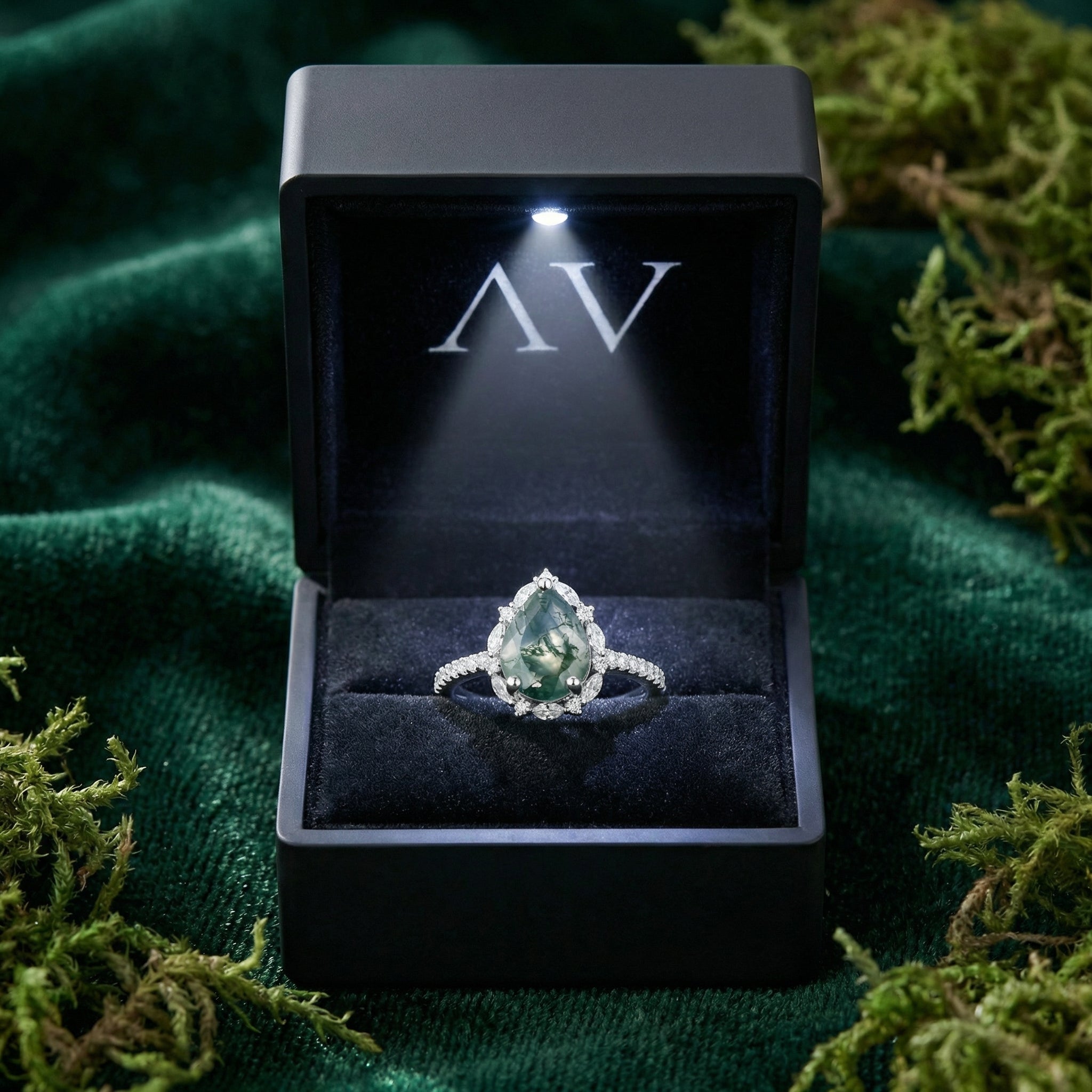 Pear cut moss agate sterling silver ring presented in a premium black LED-lit gift box on a green velvet surface.