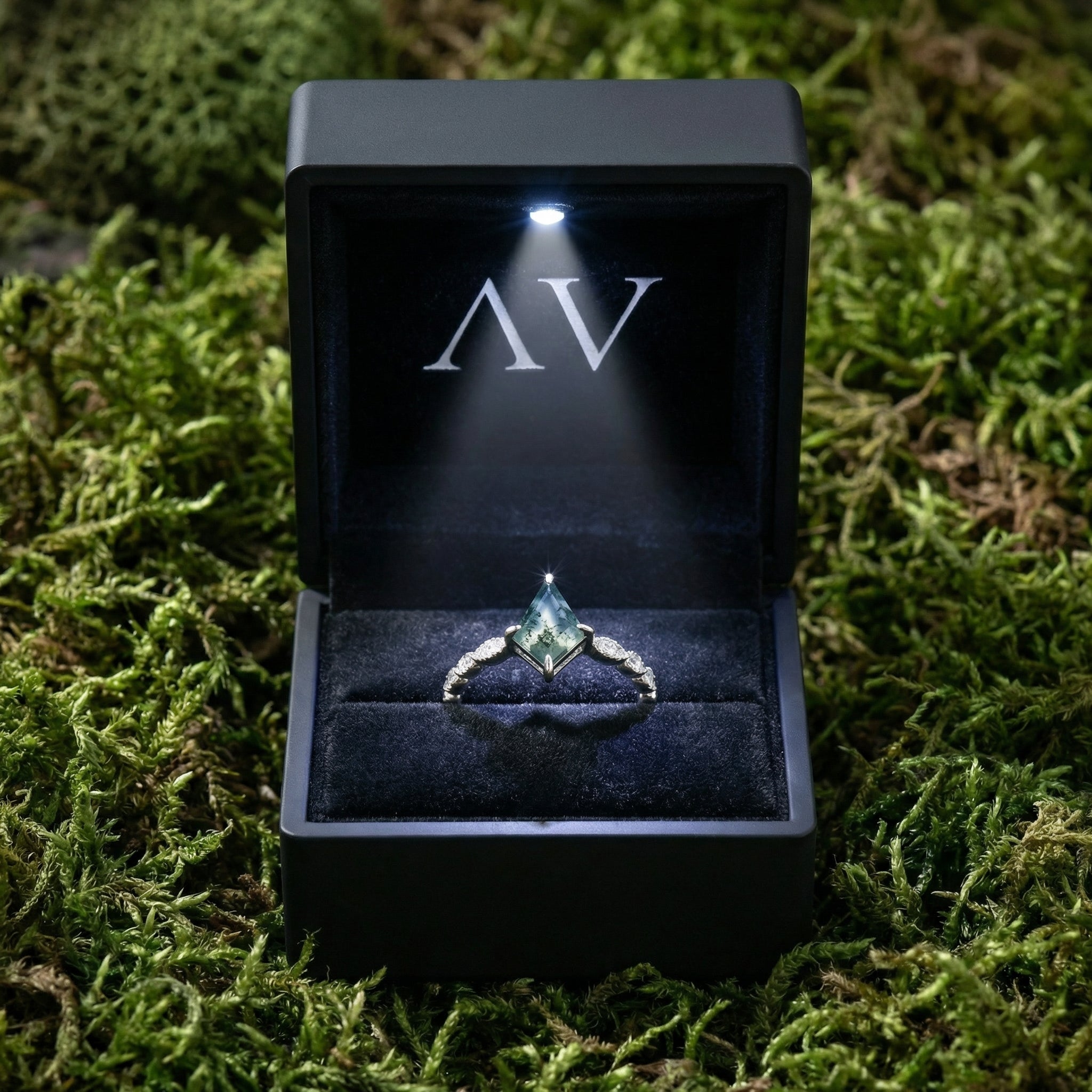 Kite cut moss agate ring in a black LED-lit gift box resting on a bed of natural green moss.