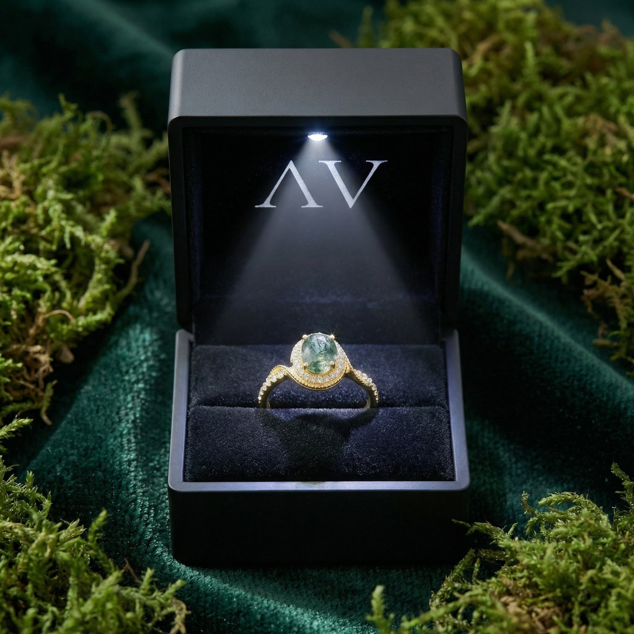 Halo oval moss agate gold ring presented in a black lighted gift box on a bed of moss.