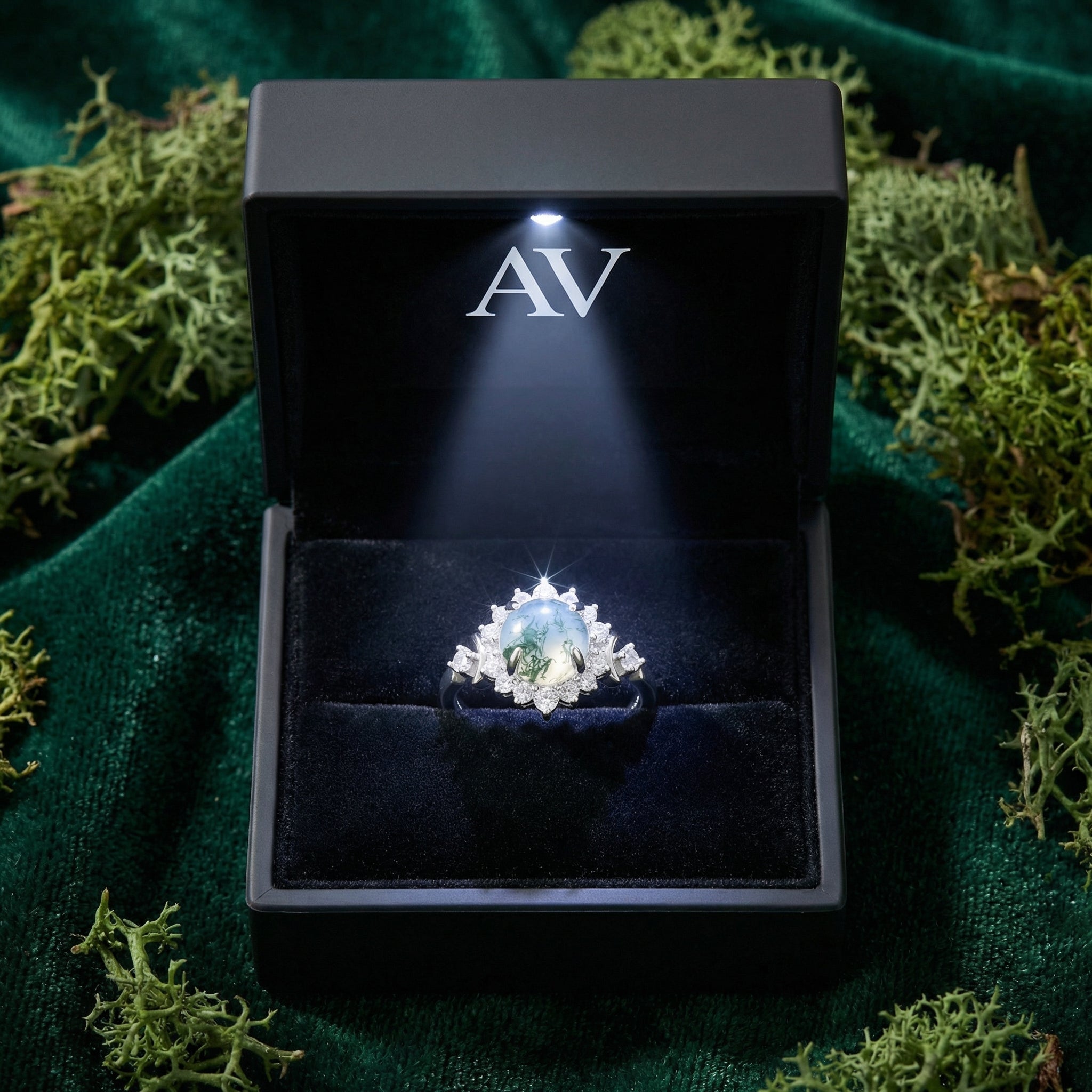 Round moss agate floral halo ring in a black LED-lit gift box on a green velvet and moss background.