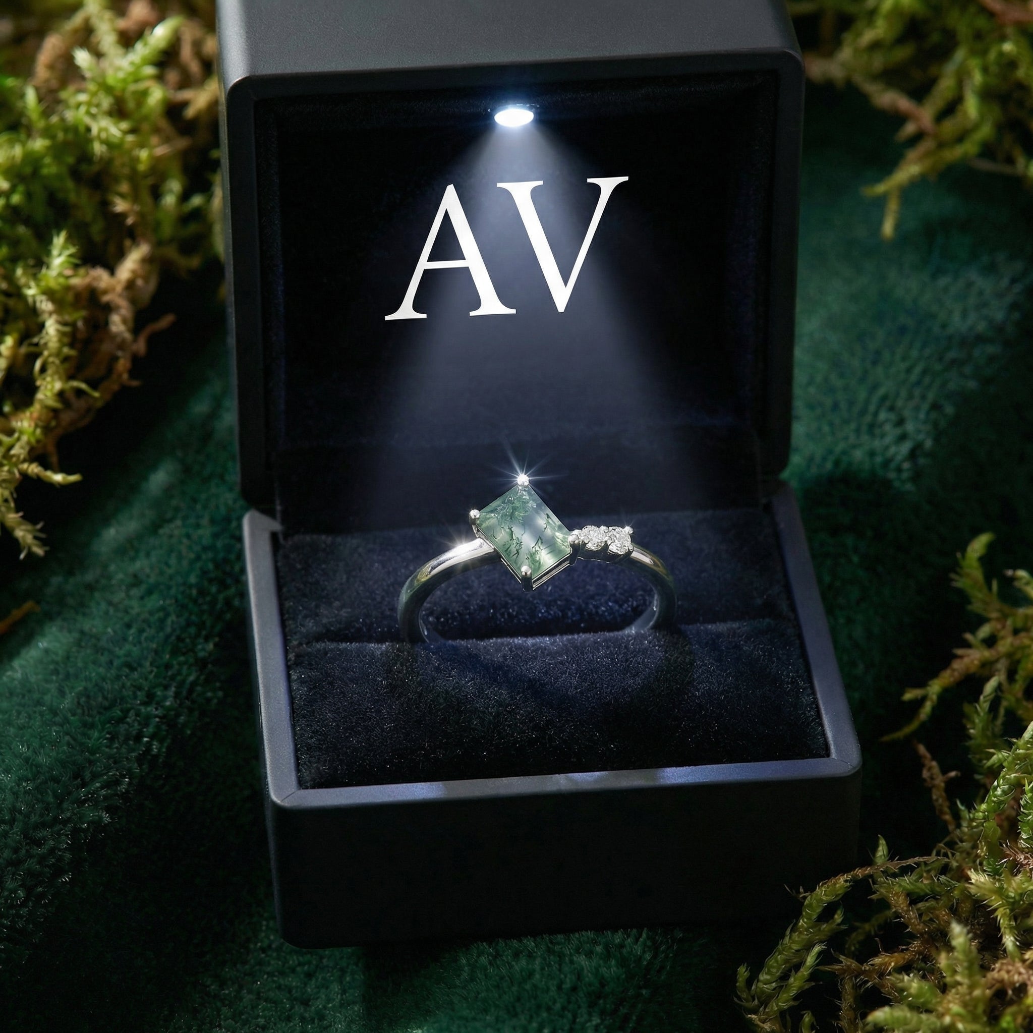 Adjustable moss agate ring displayed in a black LED lighted gift box on a green mossy surface.