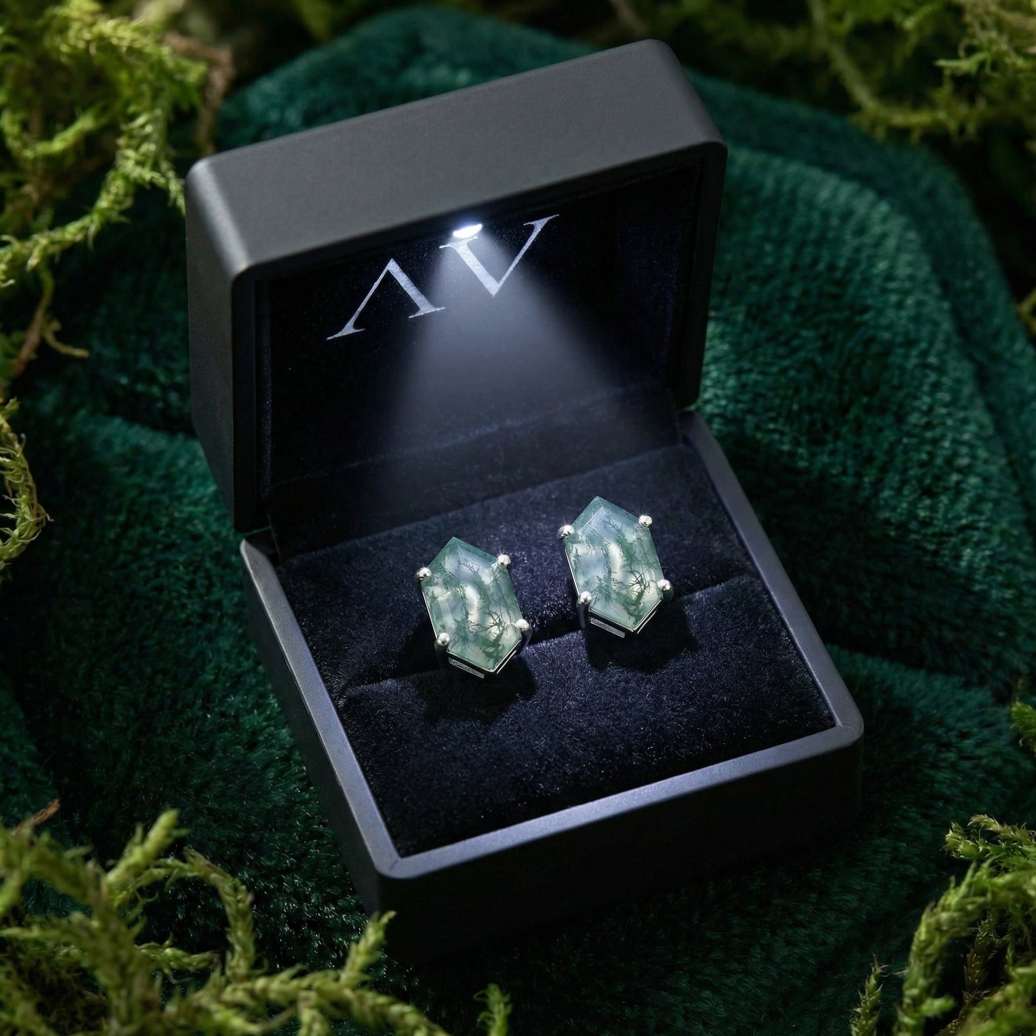 Coffin cut moss agate stud earrings in a black LED-lit gift box on a bed of green moss and velvet.