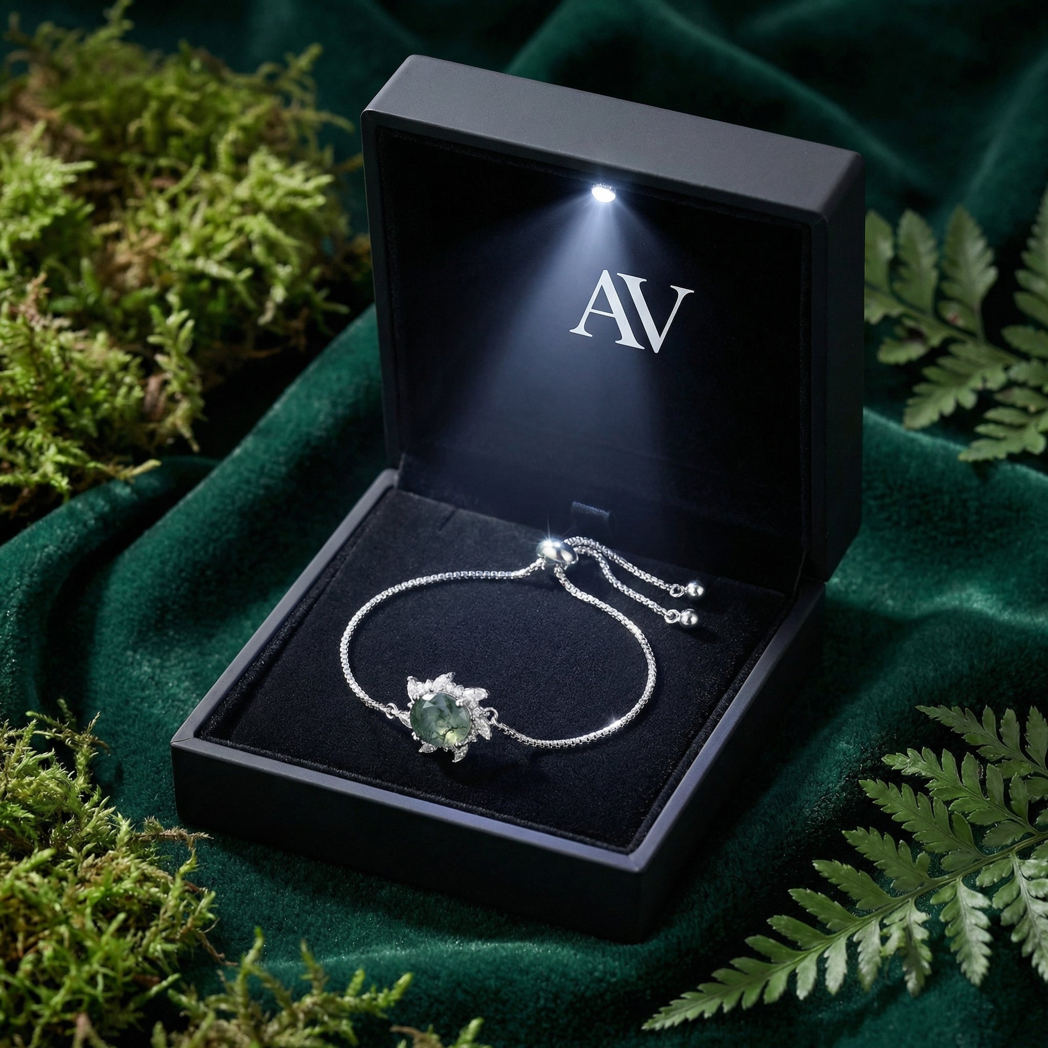 Sunburst moss agate sterling silver bracelet presented in a black LED-lit gift box on green velvet.