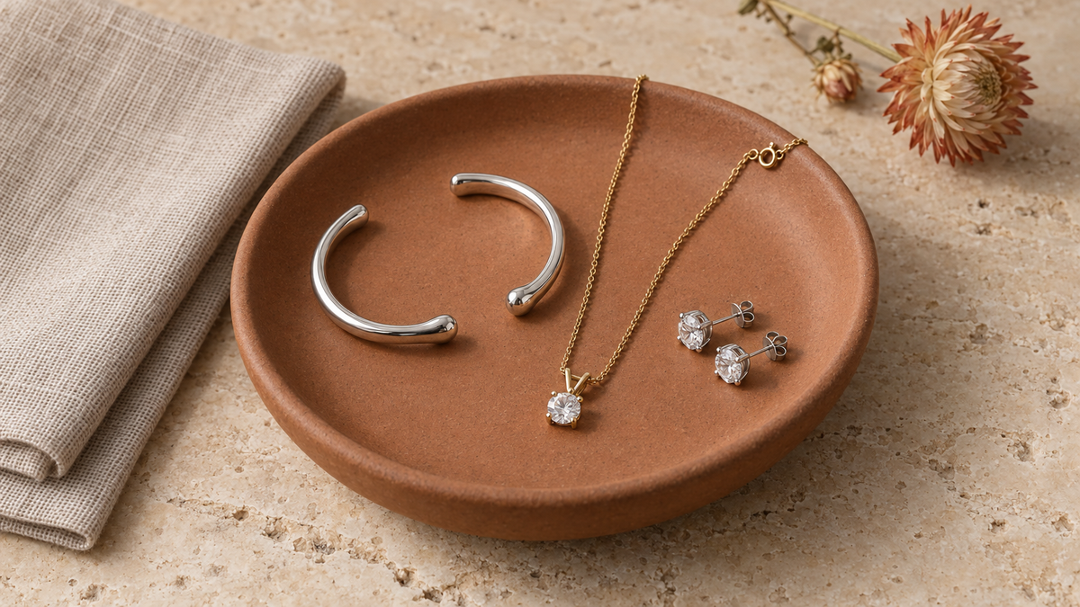 Illustrative silver-tone cuff shapes, a gold-tone pendant necklace and stud earrings on a ceramic tray; not verified depictions of listed products, stones or materials.