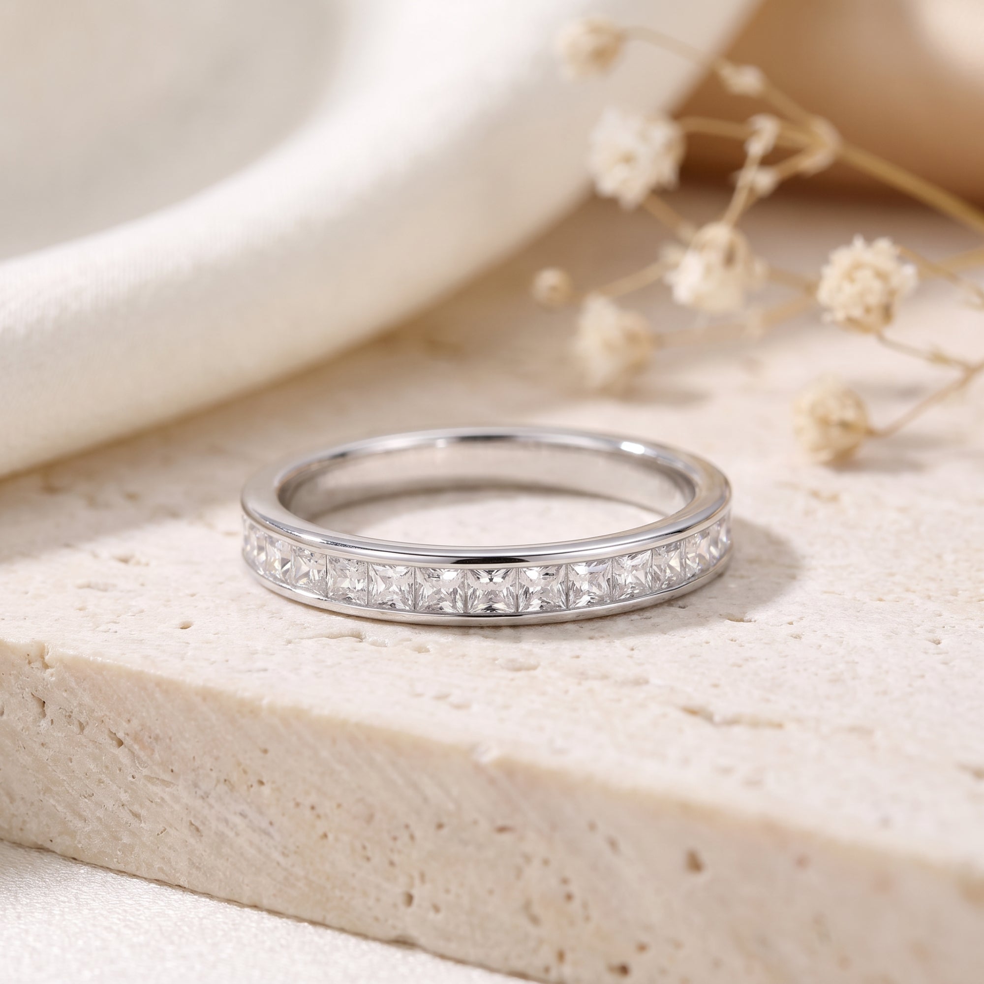 Princess cut CZ channel-set eternity ring in sterling silver on a textured stone surface.