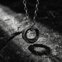 Textured silver ring pendant hanging from a link chain over a dark slate background.