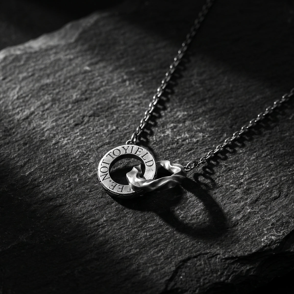 Close-up of the silver interlocking dual-ring pendant on a dark slate background.