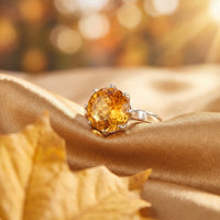 Round cut natural citrine ring in sterling silver on gold satin fabric with an autumn leaf lifestyle background.