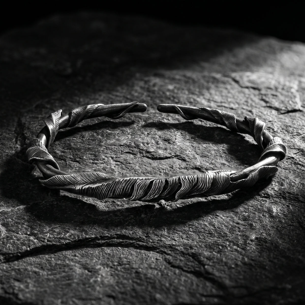 Textured silver feathered twist open cuff bracelet resting on dark slate stone.