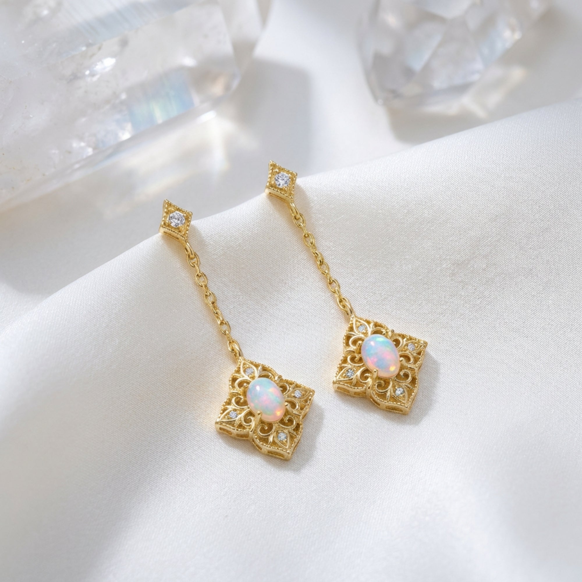 Gold-tone filigree drop earrings with oval white opals on white silk with crystal accents.