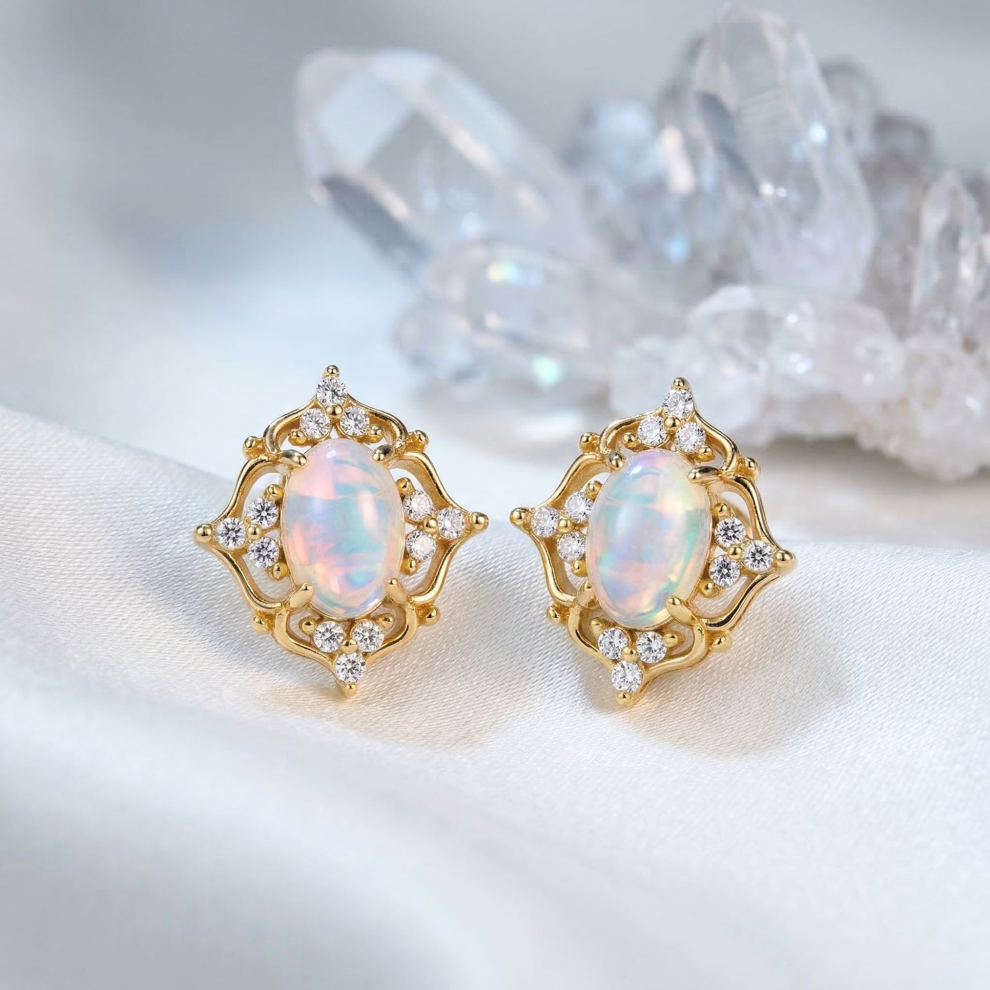 Gold-tone sterling silver earrings with oval white opals and clear accents on white fabric with crystals.