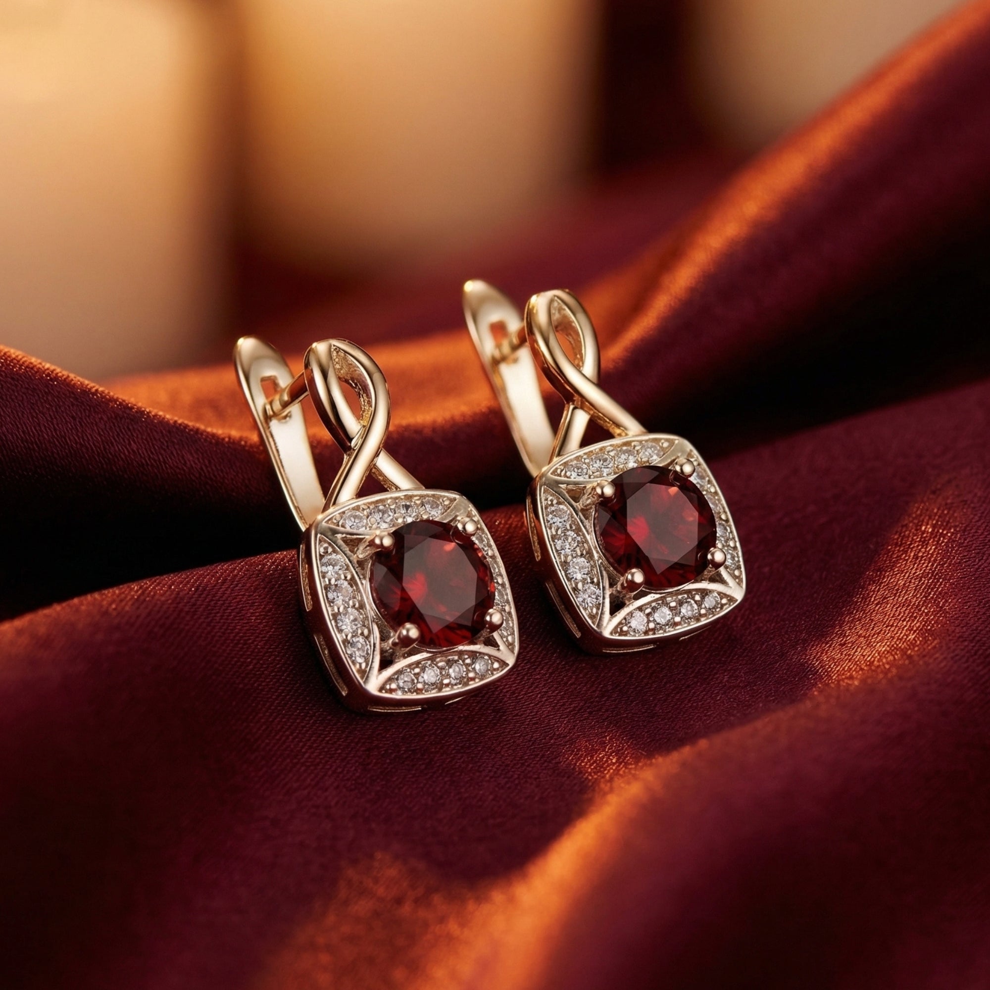 Round-cut garnet drop earrings in sterling silver with a zircon halo, glowing under warm light on burgundy silk.